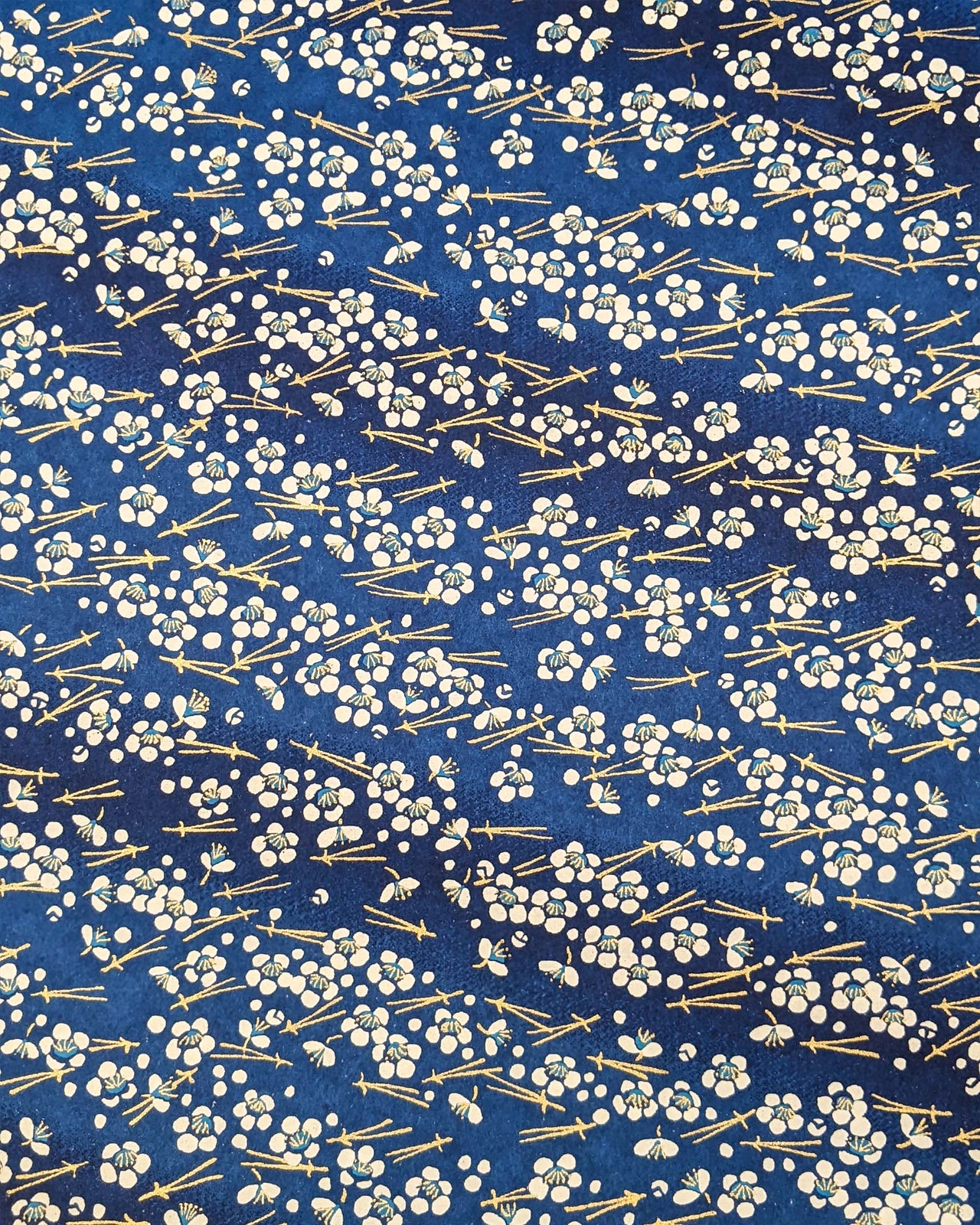 Japanese chiyogami featuring small white plum blossoms & matsuba (pine needles) on a blue background with metallic gold accents.