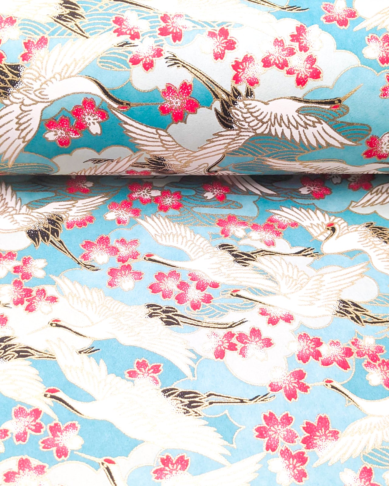 Japanese chiyogami paper featuring flying white cranes and pink cherry blossoms a light blue background with metallic gold accents.