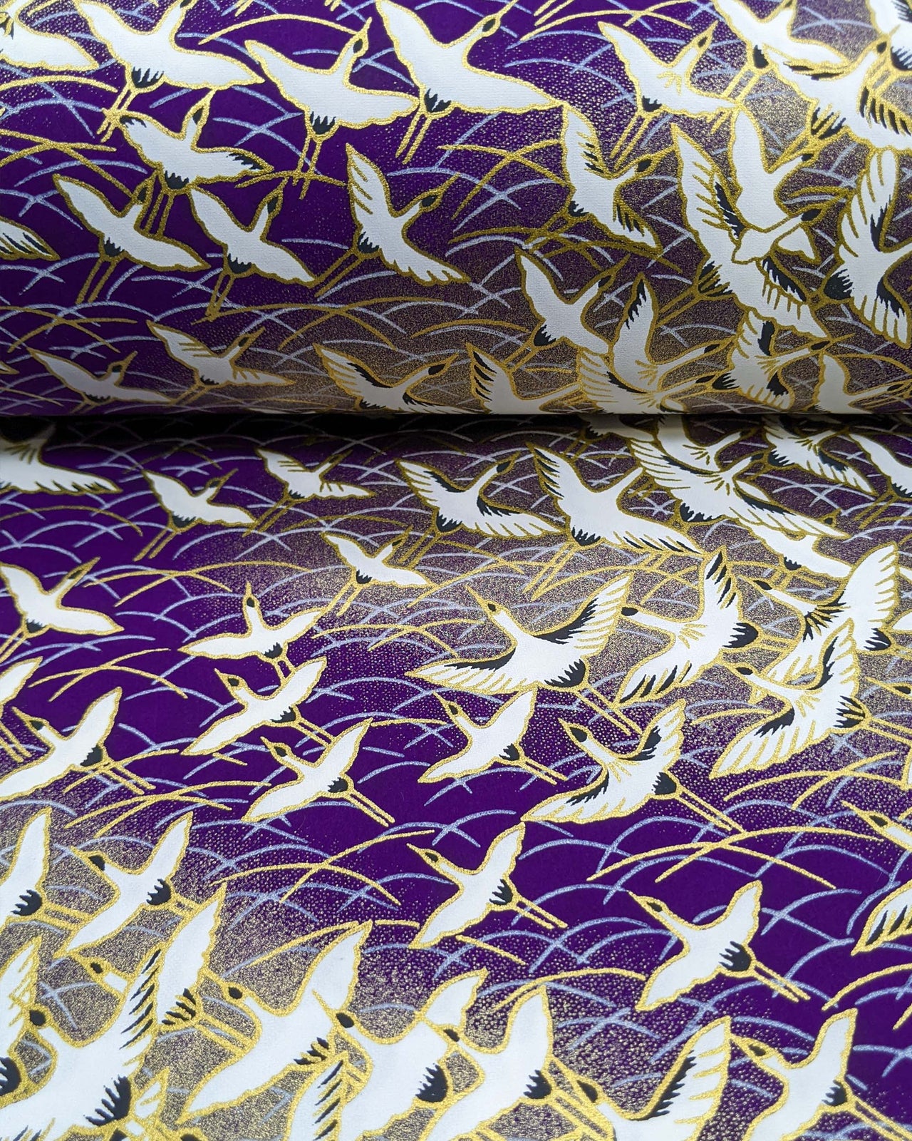 Japanese chiyogami paper featuring white flying cranes in zigzagging on a gold & purple background with metallic gold accents.