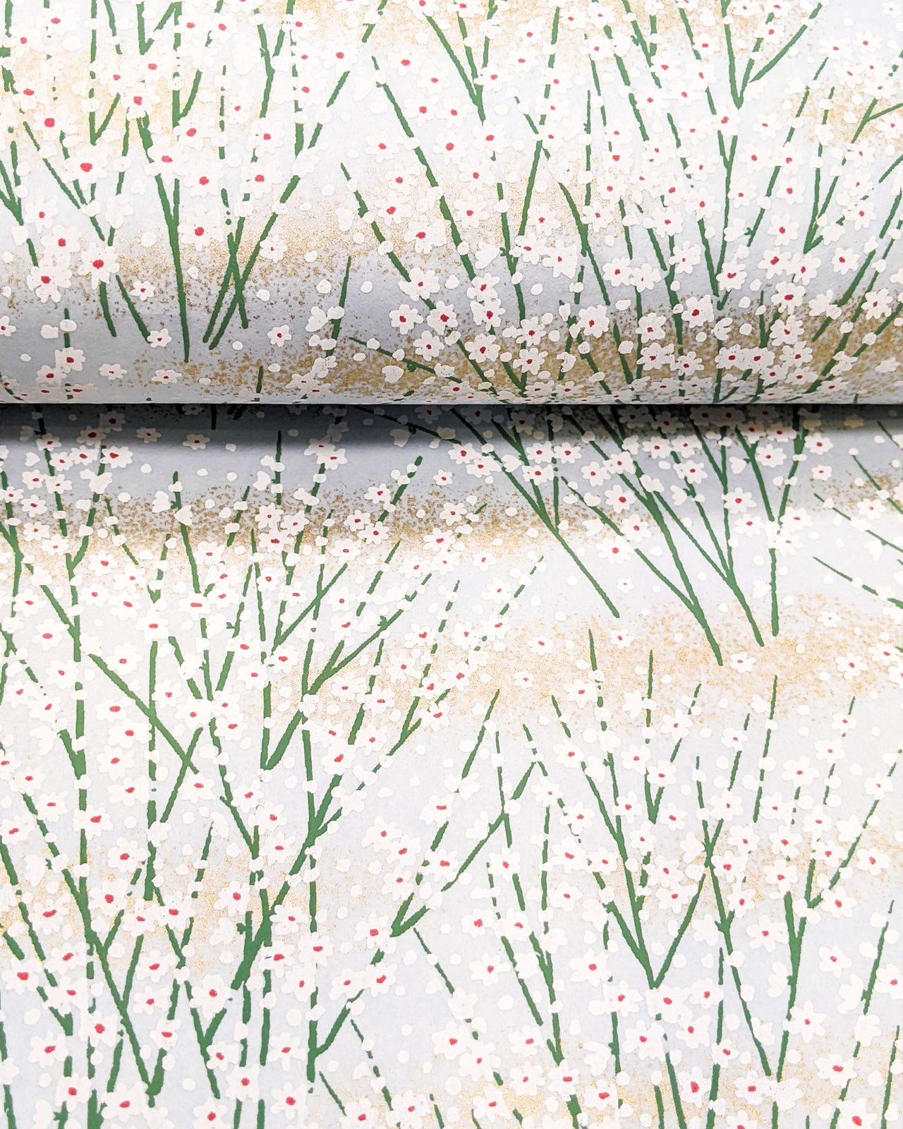Japanese chiyogami paper featuring small white flower bushes over a light blue background with metallic gold accents.