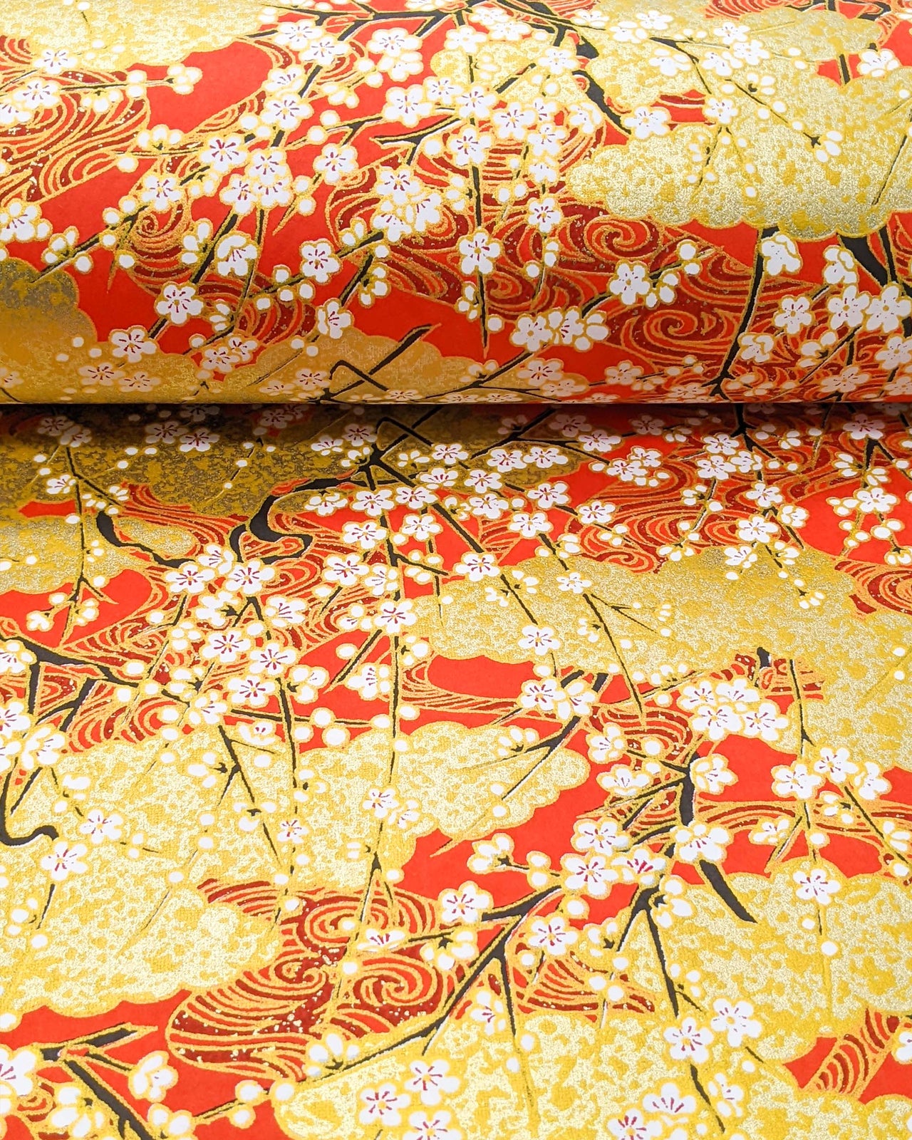 Japanese chiyogami featuring white plum blossom branches on a red and gold background with metallic gold accents.