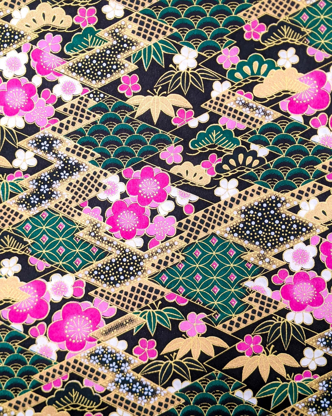 Japanese chiyogami paper featuring pink & white plum blossoms on a black & green background with metallic gold accents.