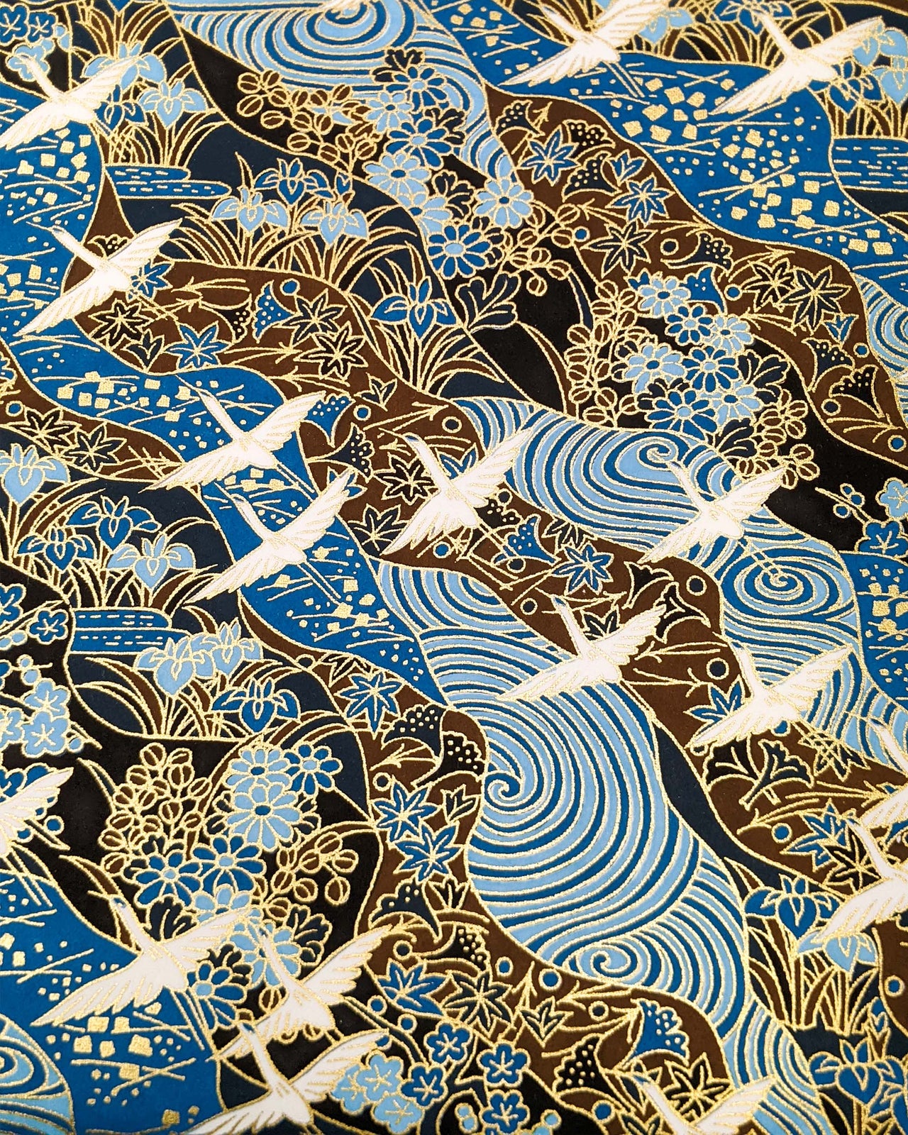 Japanese chiyogami paper featuring flying white cranes on a floral blue and brown background with metallic gold details