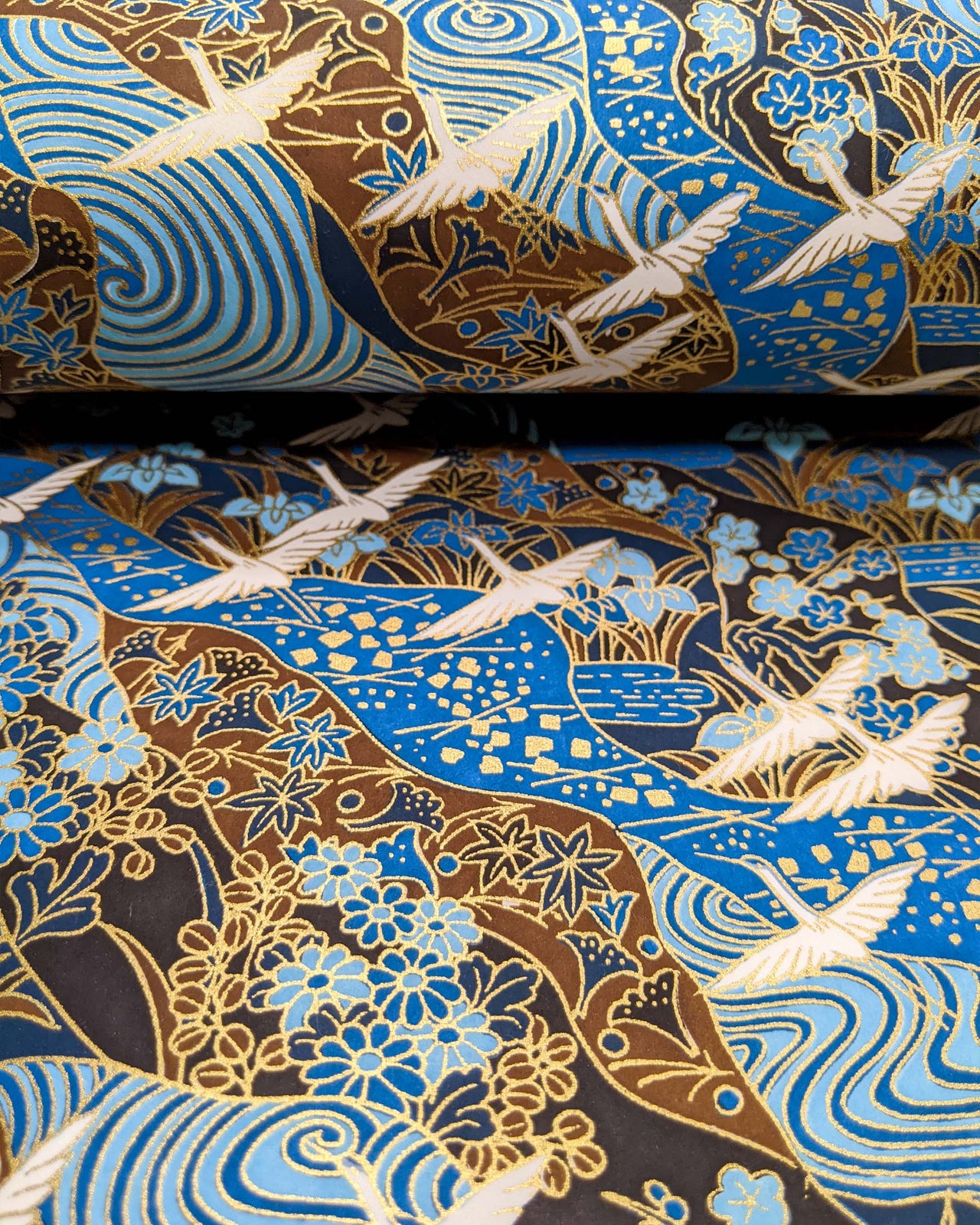 Japanese chiyogami paper featuring flying white cranes on a floral blue and brown background with metallic gold details