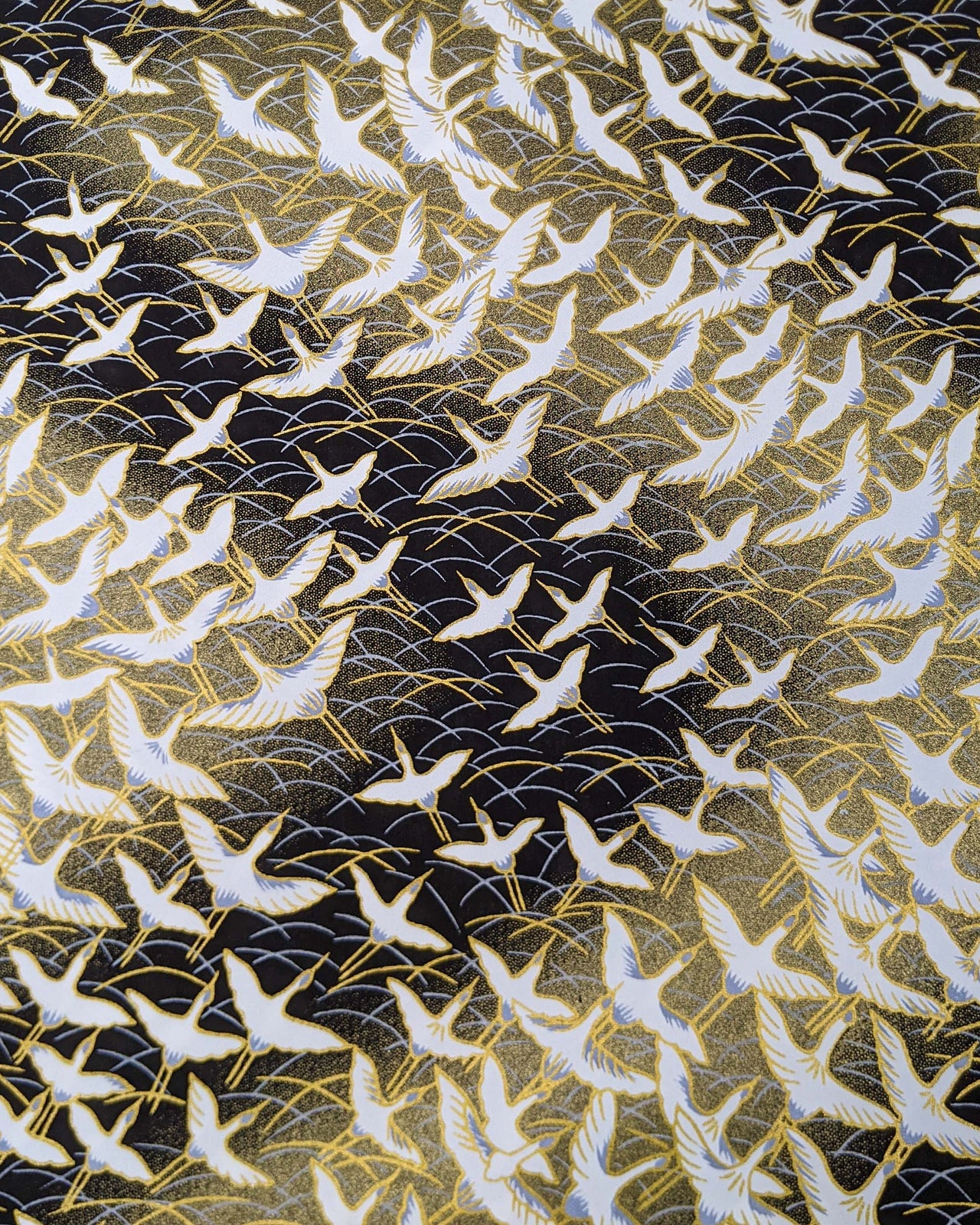 Japanese chiyogami paper featuring white flying cranes in a zigzag formation on a black and gold background with metallic gold and silver details.