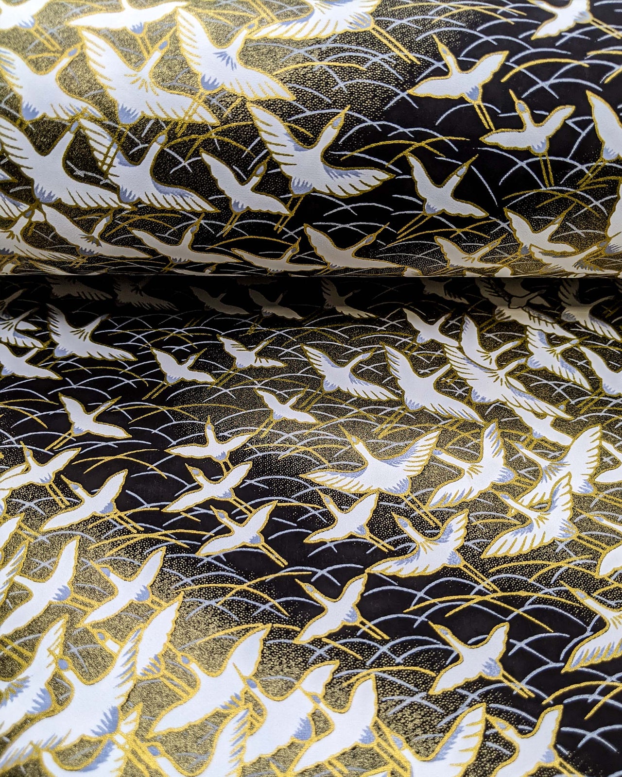 Japanese chiyogami paper featuring white flying cranes in a zigzag formation on a black and gold background with metallic gold and silver details.