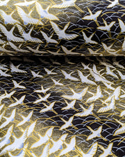 Japanese chiyogami paper featuring white flying cranes in a zigzag formation on a black and gold background with metallic gold and silver details.