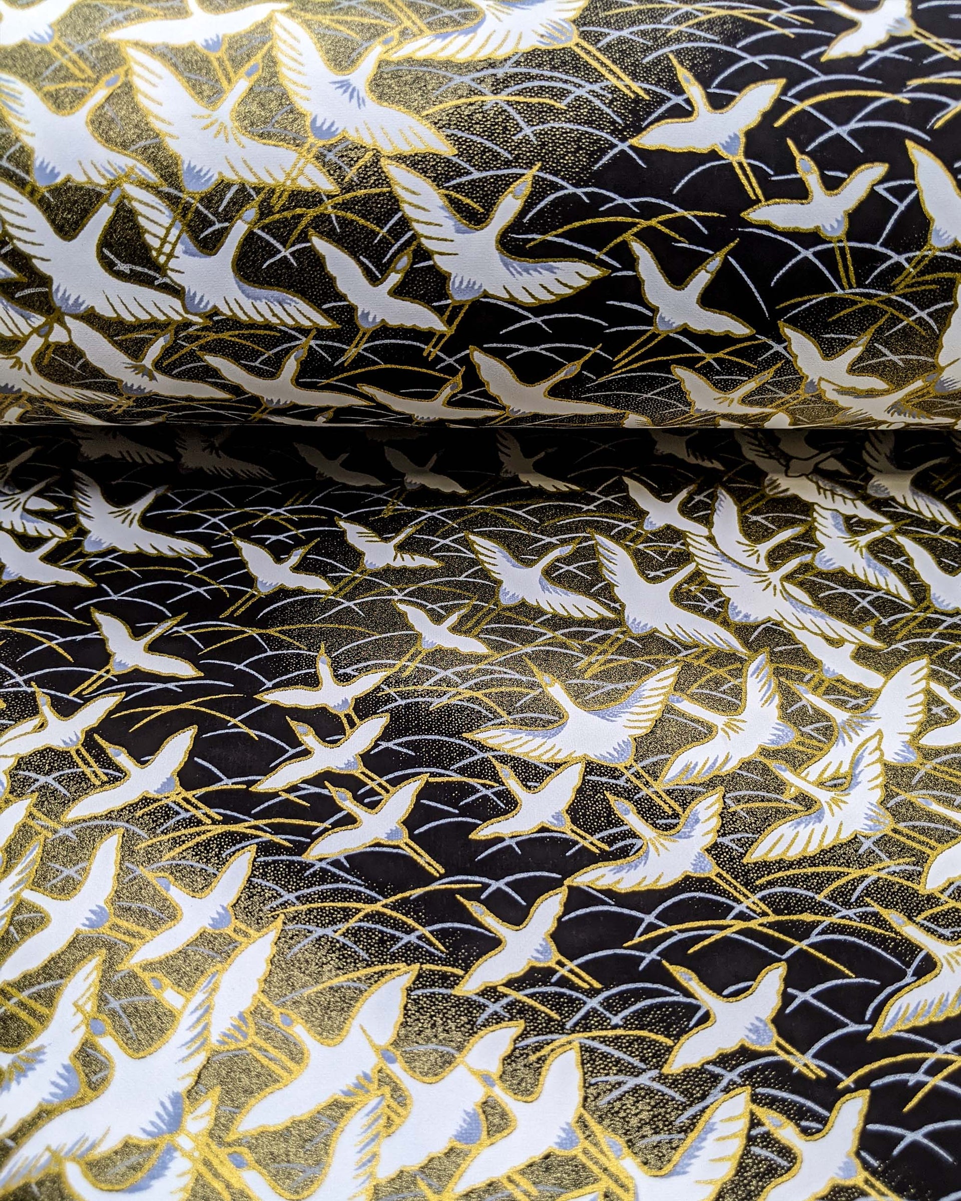 Japanese chiyogami paper featuring white flying cranes in a zigzag formation on a black and gold background with metallic gold and silver details.