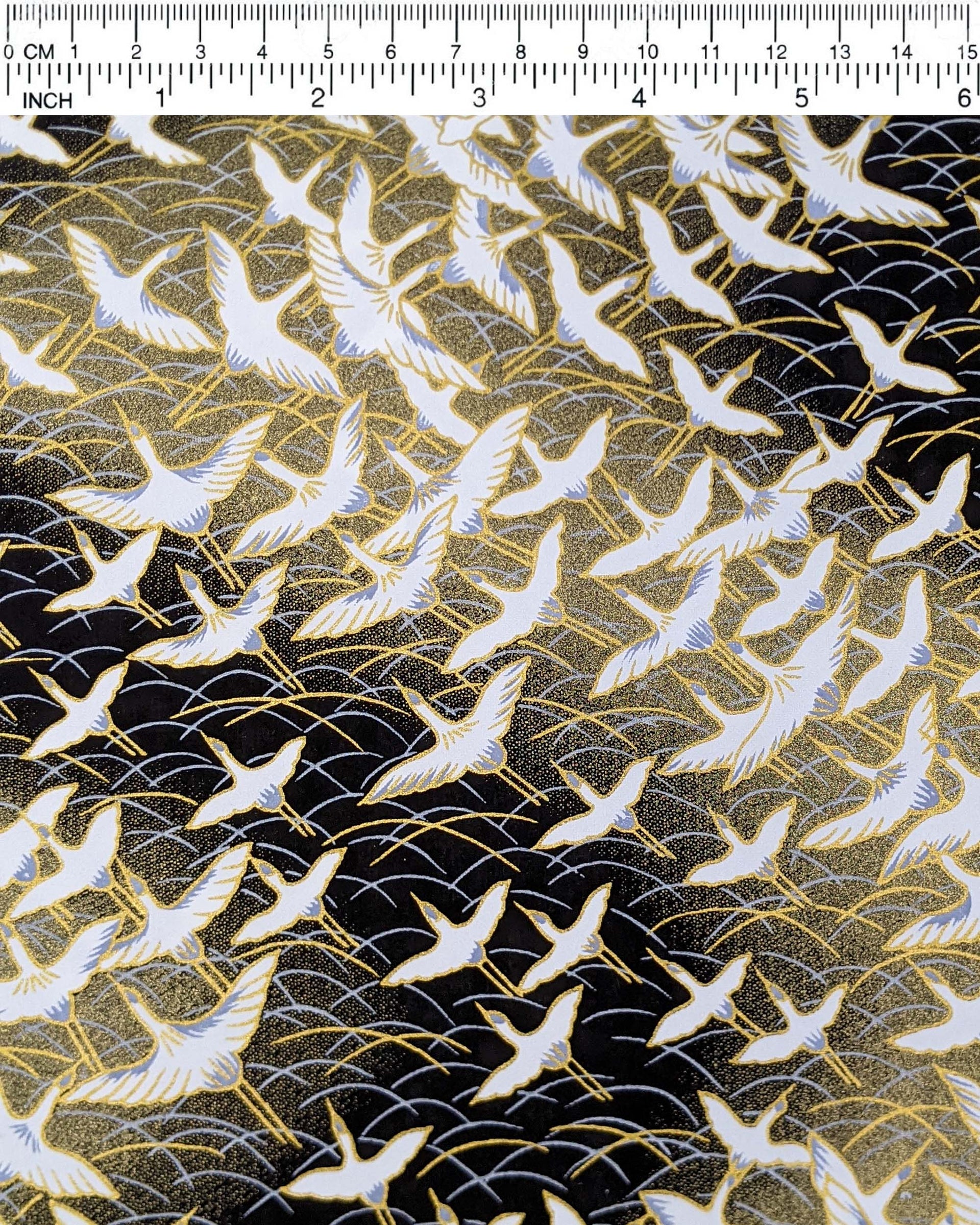 Japanese chiyogami paper featuring white flying cranes in a zigzag formation on a black and gold background with metallic gold and silver details.