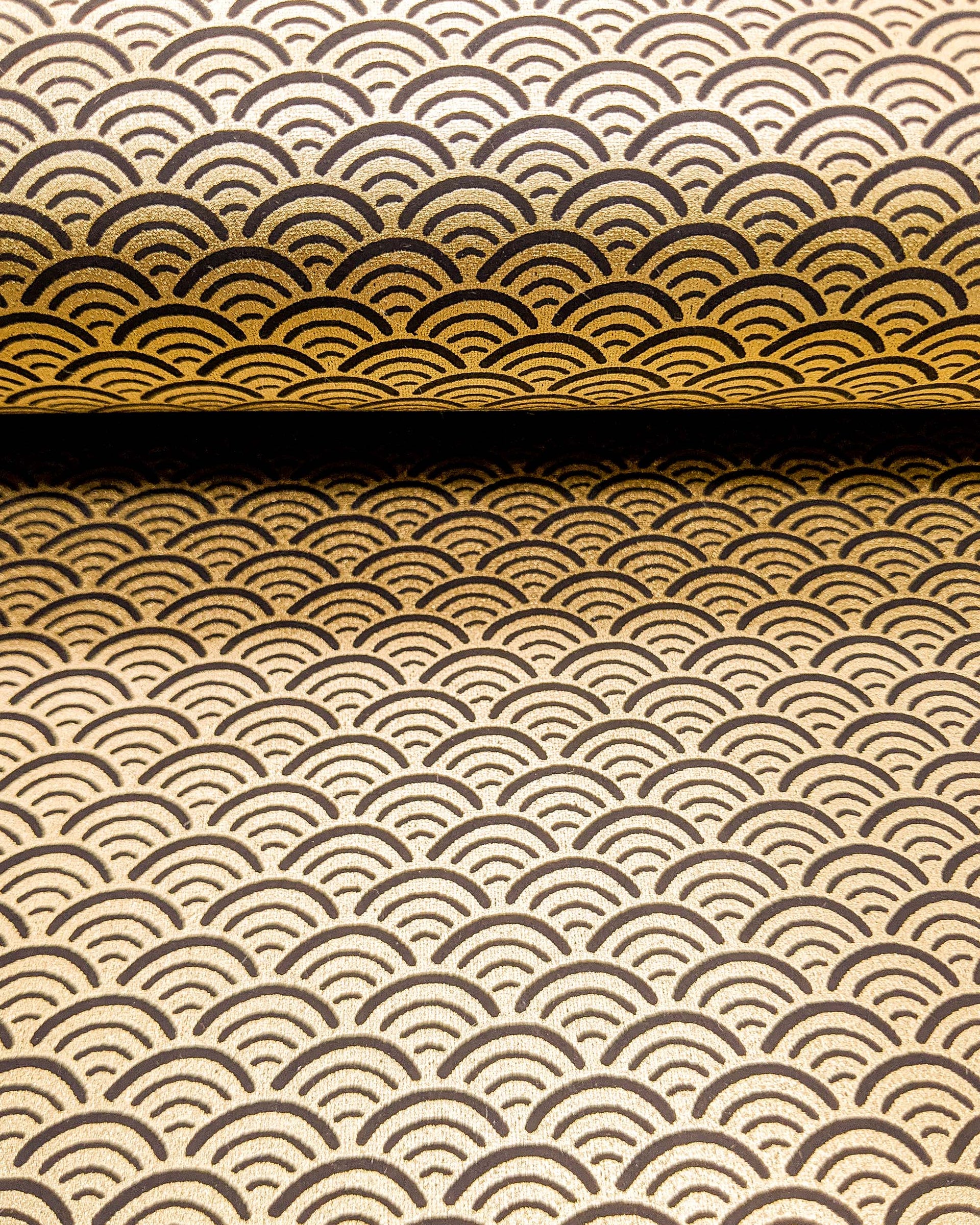 Japanese chiyogami paper featuring a traditional black and metallic gold seigaiha (wave crests) pattern.