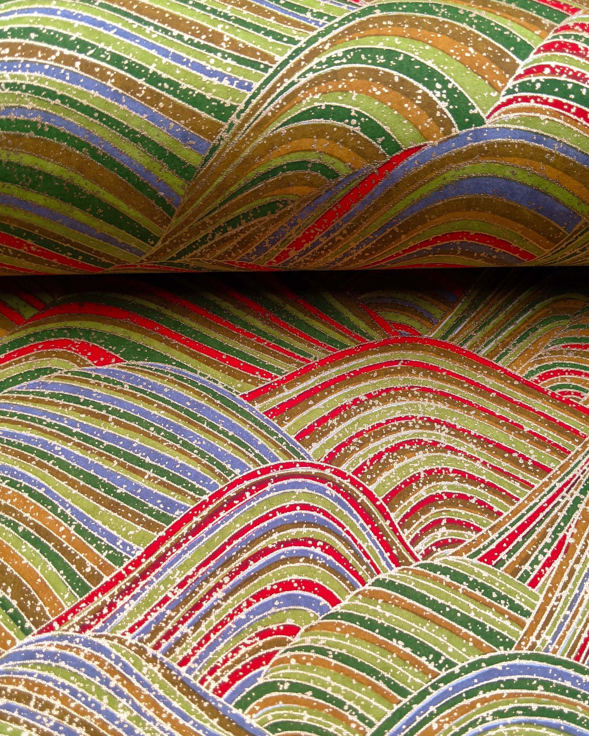 Japanese chiyogami paper featuring striped rolling hills in a mix of green, red, brown,and gray with metallic gold details.