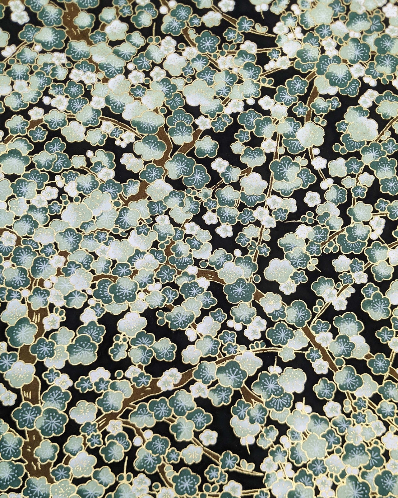 Japanese chiyogami paper featuring green plum blossom trees with brown branches on a black background with metallic gold details.