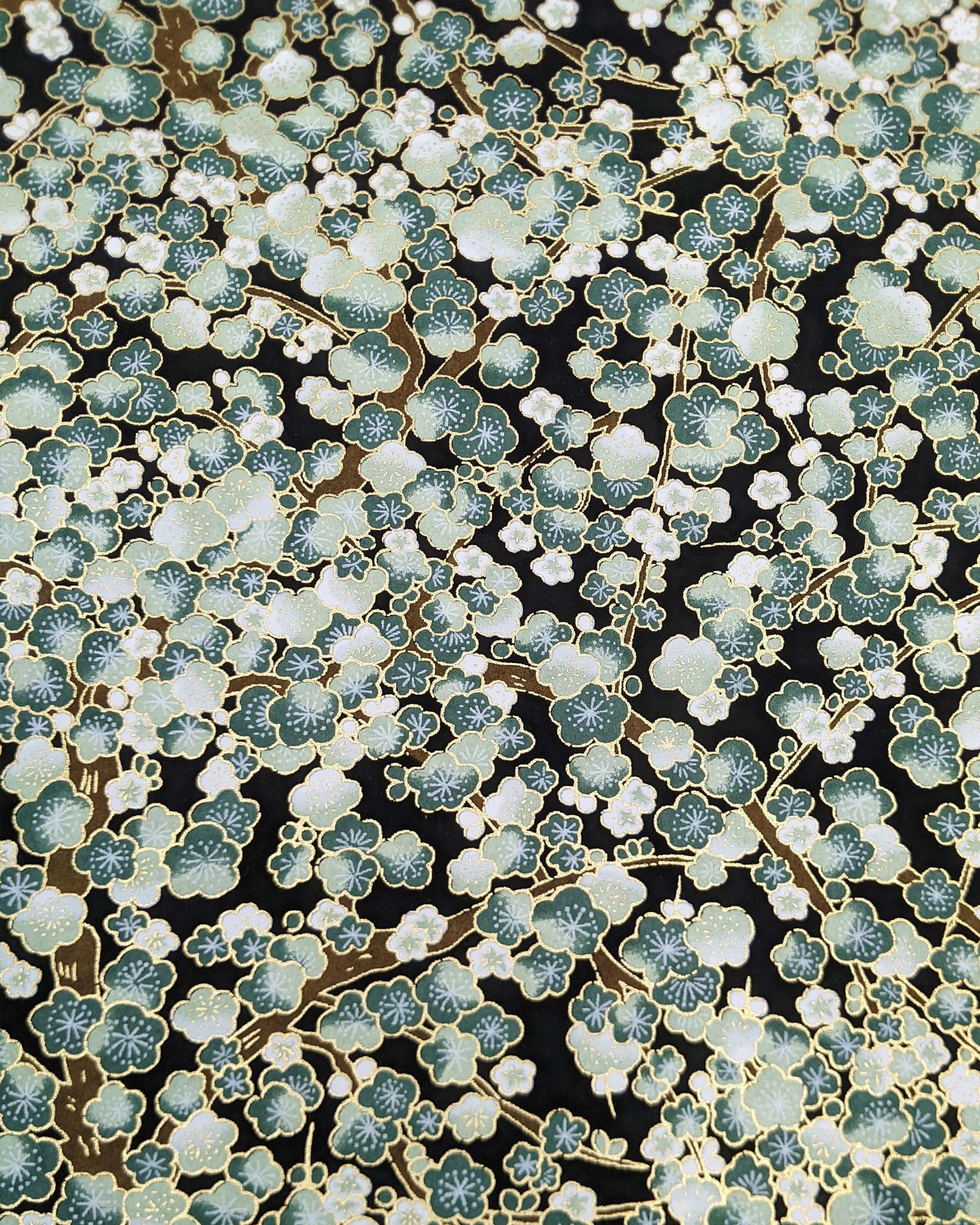 Japanese chiyogami paper featuring green plum blossom trees with brown branches on a black background with metallic gold details.