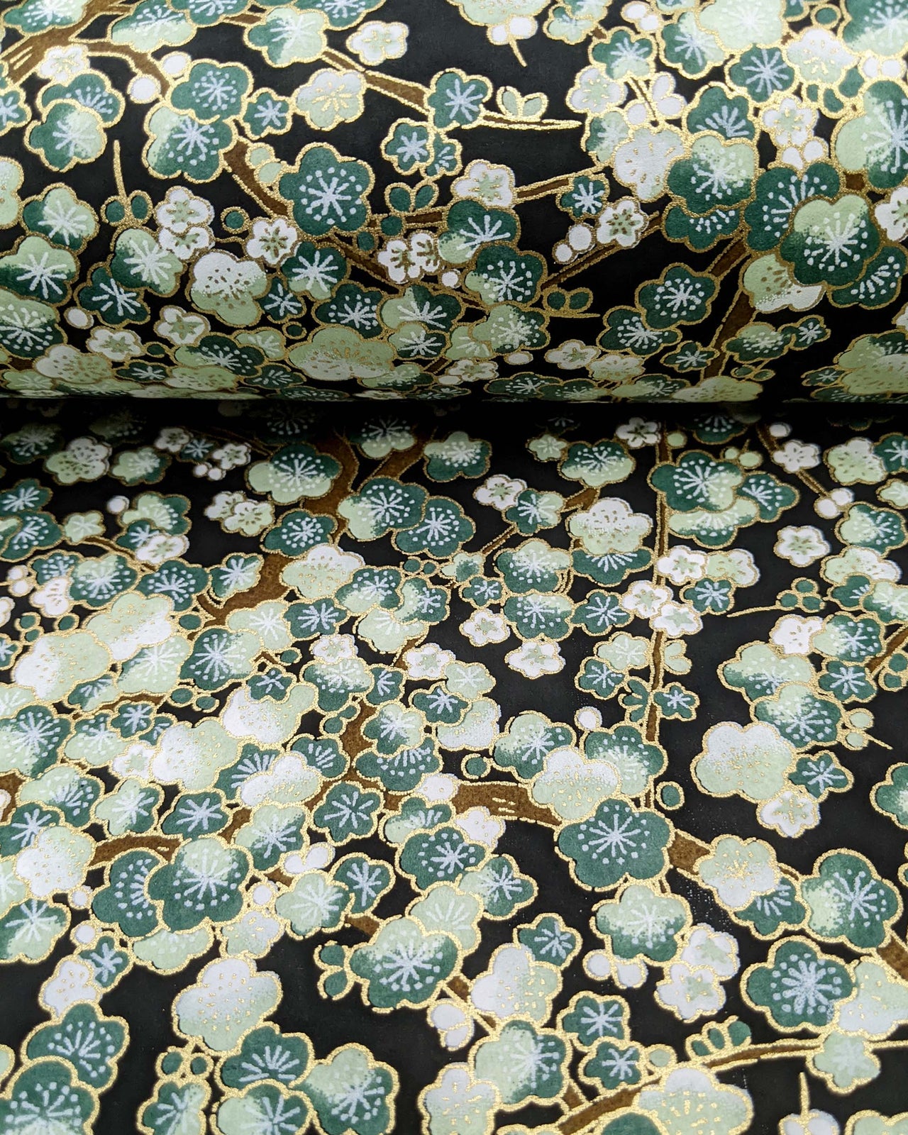 Japanese chiyogami paper featuring green plum blossom trees with brown branches on a black background with metallic gold details.