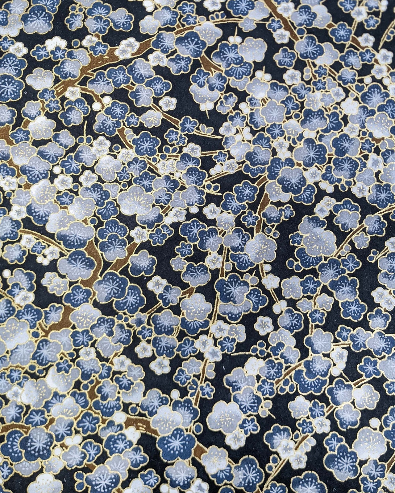 Japanese chiyogami paper featuring blue and gray plum blossom trees with brown branches on a dark blue background with metallic gold details.