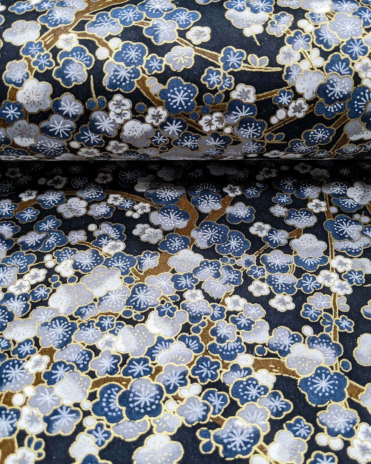 Japanese chiyogami paper featuring blue and gray plum blossom trees with brown branches on a dark blue background with metallic gold details.