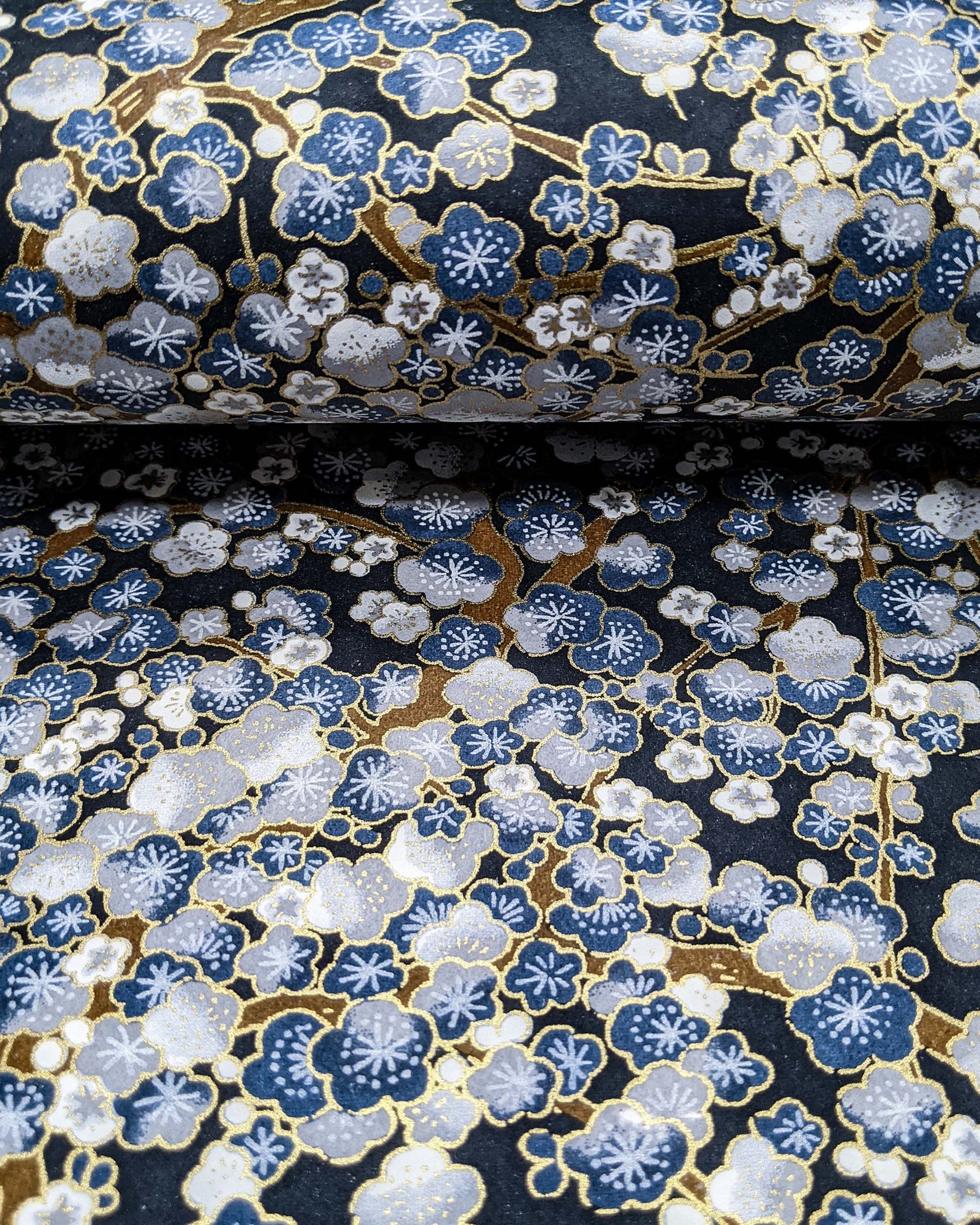 Japanese chiyogami paper featuring blue and gray plum blossom trees with brown branches on a dark blue background with metallic gold details.