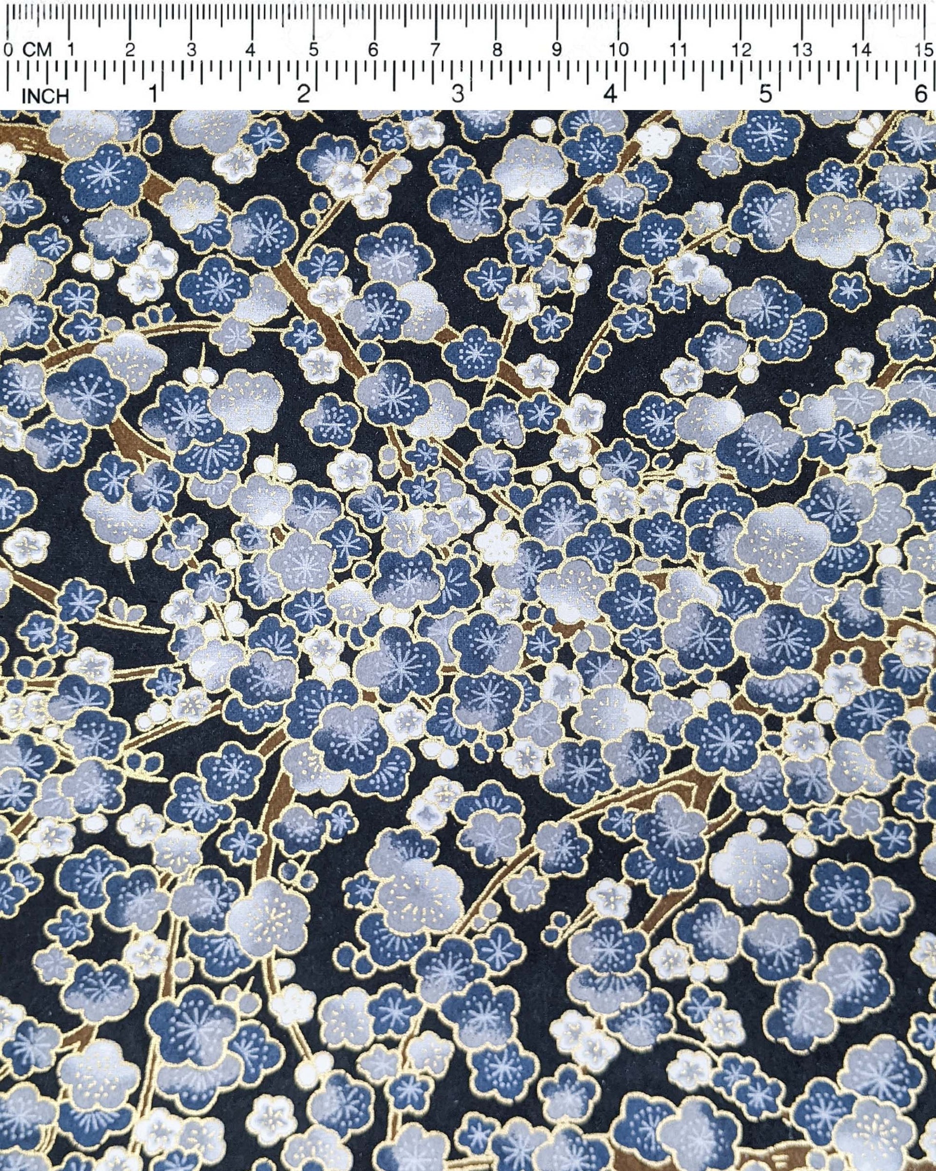 Japanese chiyogami paper featuring blue and gray plum blossom trees with brown branches on a dark blue background with metallic gold details.