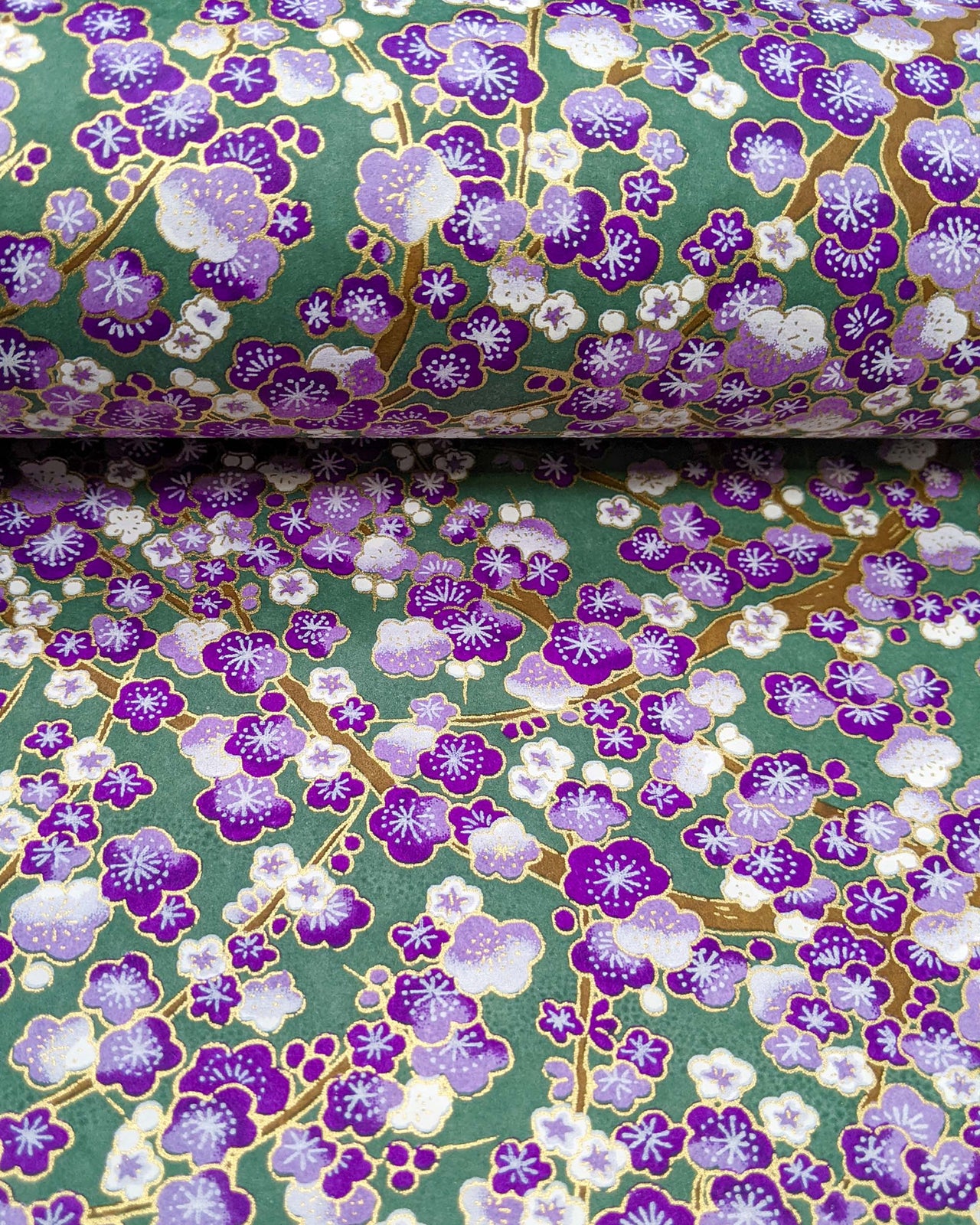 Japanese chiyogami paper featuring purple and white plum blossom trees with brown branches on a purple background with metallic gold details.
