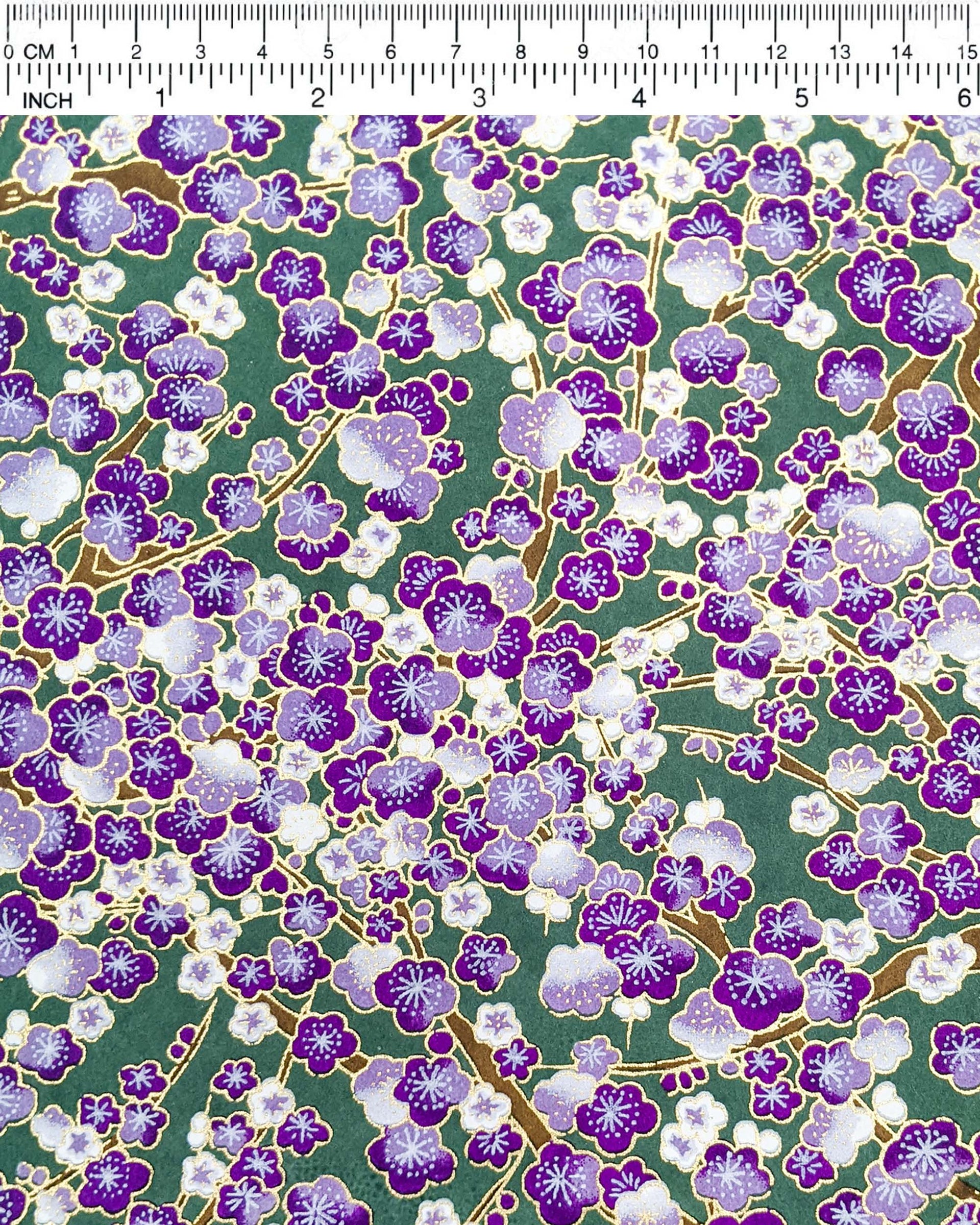 Japanese chiyogami paper featuring purple and white plum blossom trees with brown branches on a purple background with metallic gold details.