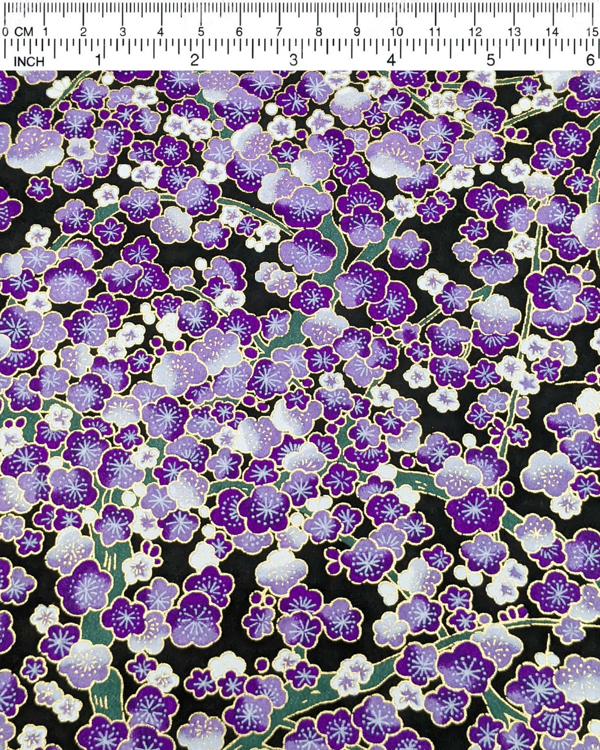 Japanese chiyogami paper featuring purple and white plum blossom trees with green branches on a black background with metallic gold details, shown next to a ruler for size reference.
