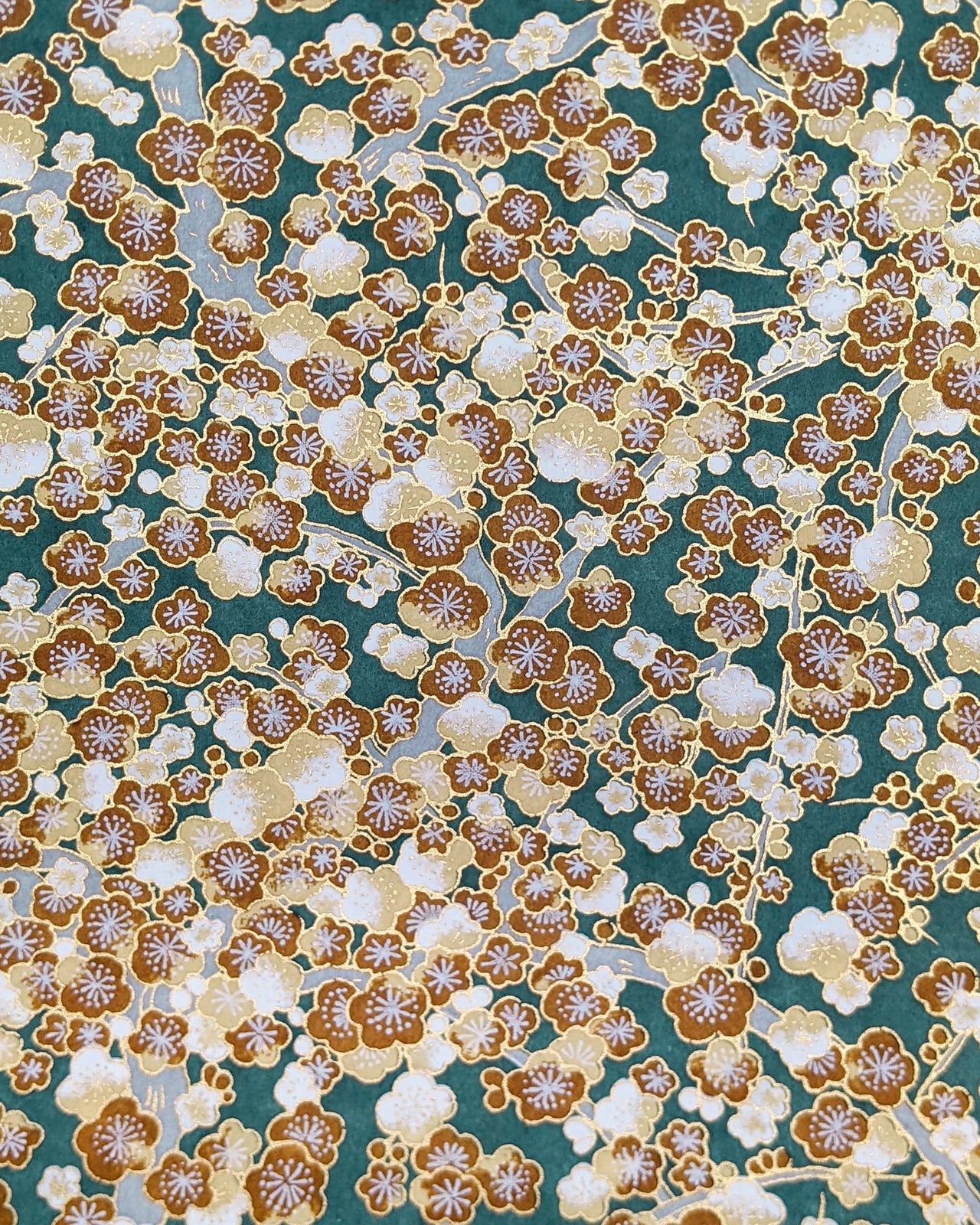 Japanese chiyogami paper featuring brown and white plum blossom trees with gray branches on a green background with metallic gold details.