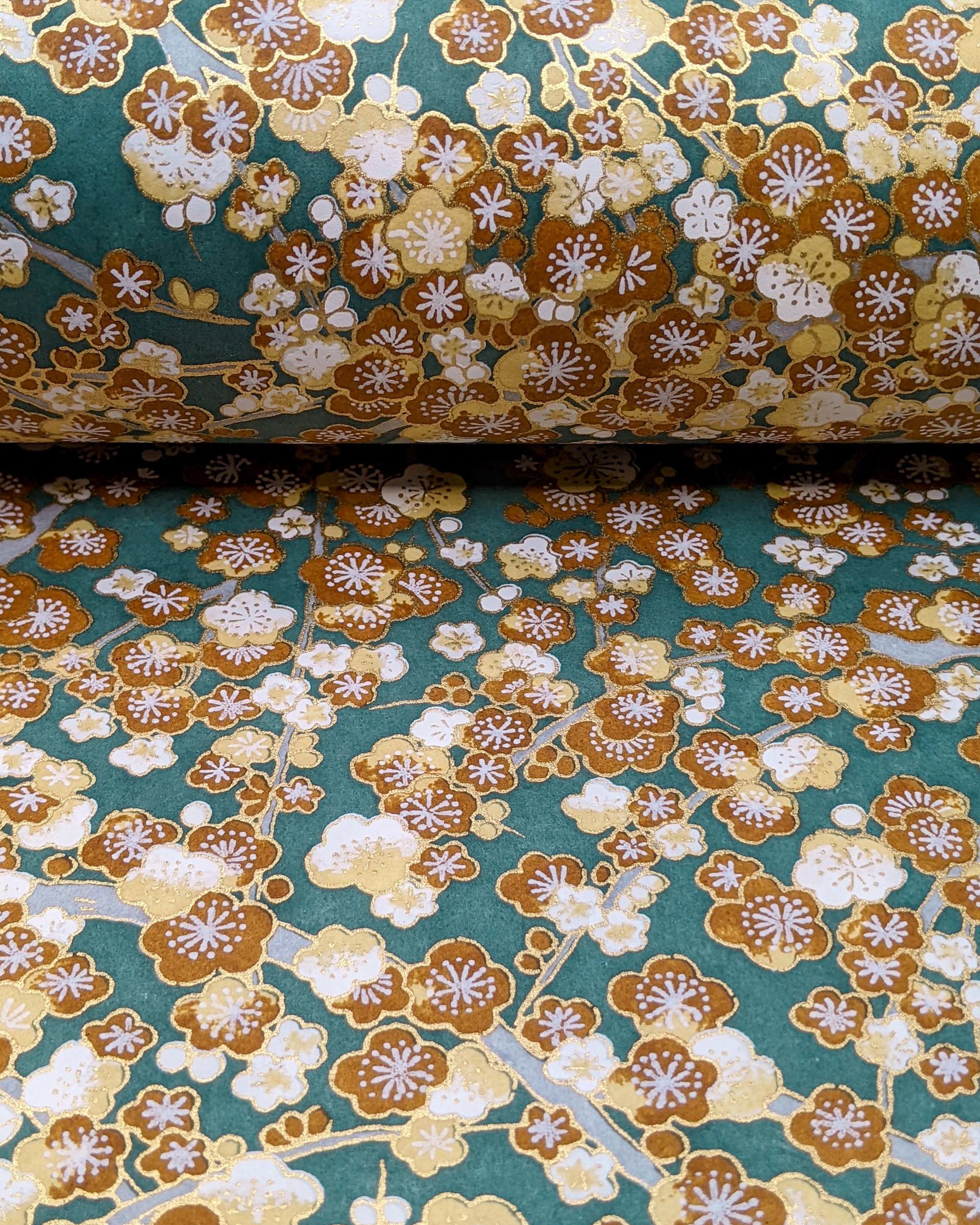 Japanese chiyogami paper featuring brown and white plum blossom trees with gray branches on a green background with metallic gold details.