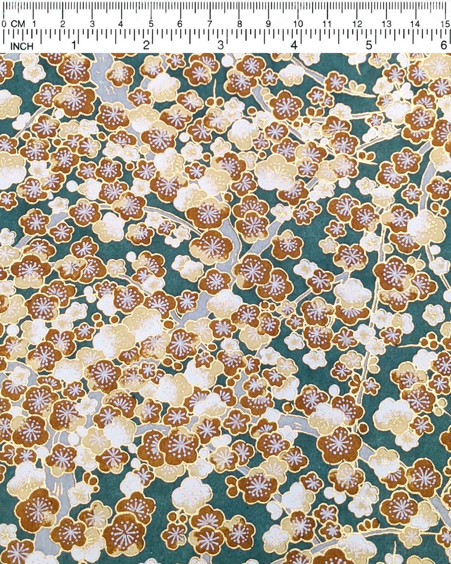 Japanese chiyogami paper featuring brown and white plum blossom trees with gray branches on a green background with metallic gold details.