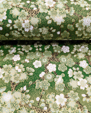 Japanese chiyogami paper featuring green and white cherry and plum blossoms with black branches on a green background with metallic gold details. 