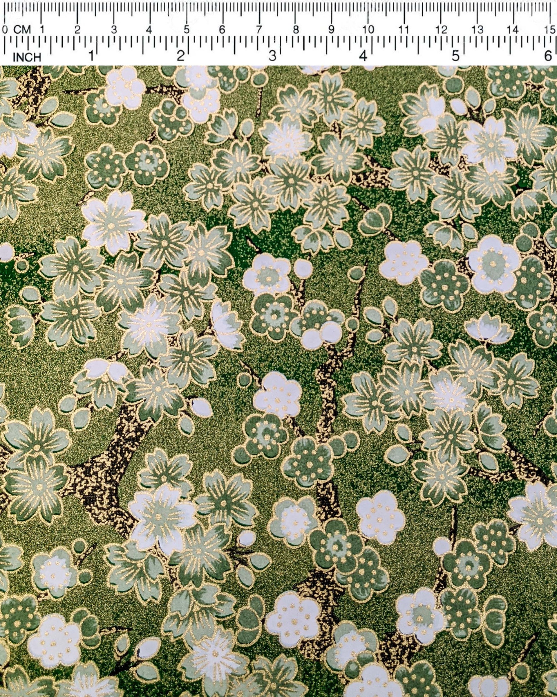 Japanese chiyogami paper featuring green and white cherry and plum blossoms with black branches on a green background with metallic gold details. 