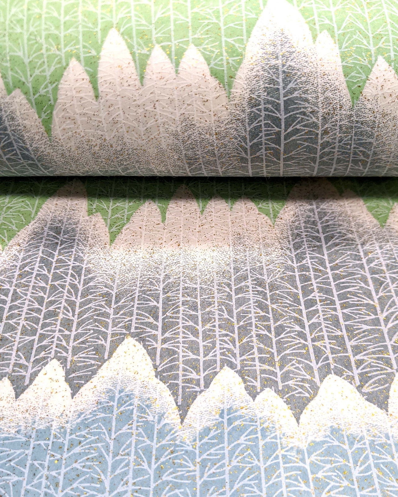 Japanese chiyogami paper featuring white snow-capped mountains with a forest of trees on a gray, blue, and green background with metallic gold glitter details.
