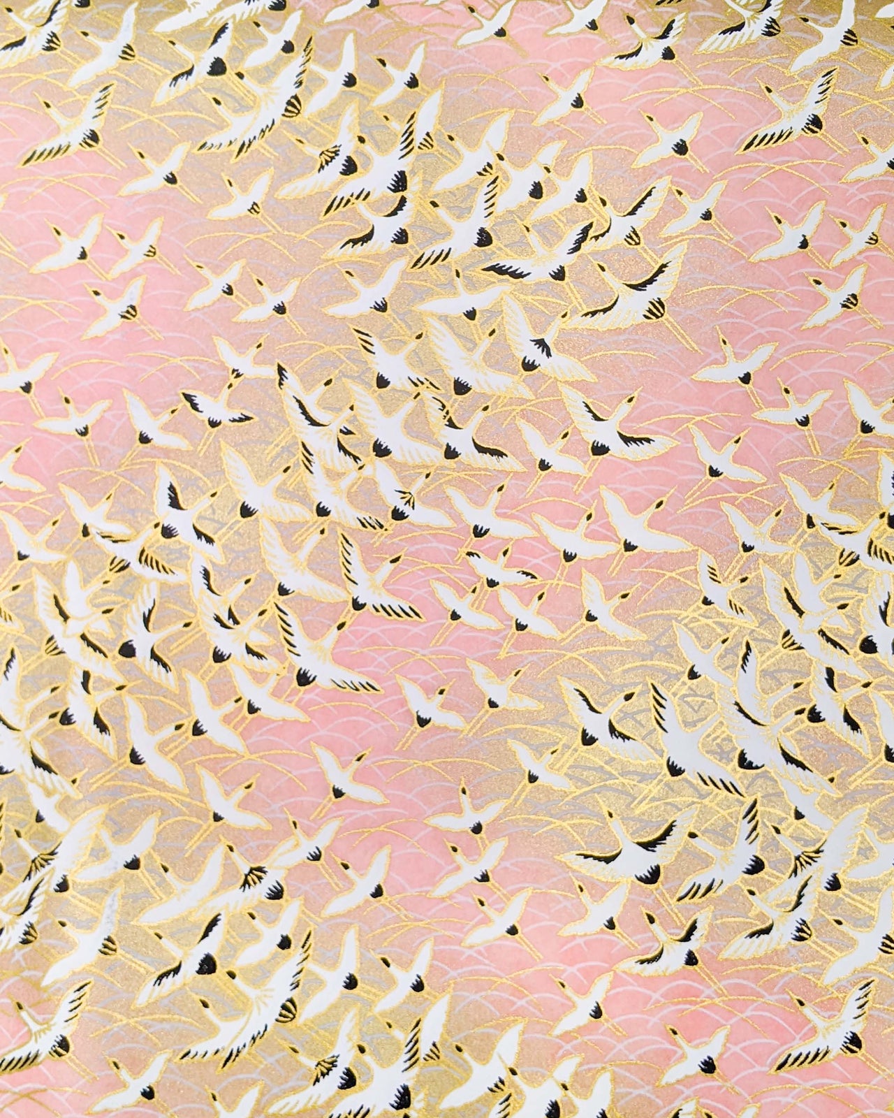 Japanese chiyogami paper featuring white flying cranes in a zigzag formation on a light pink background with metallic gold details.
