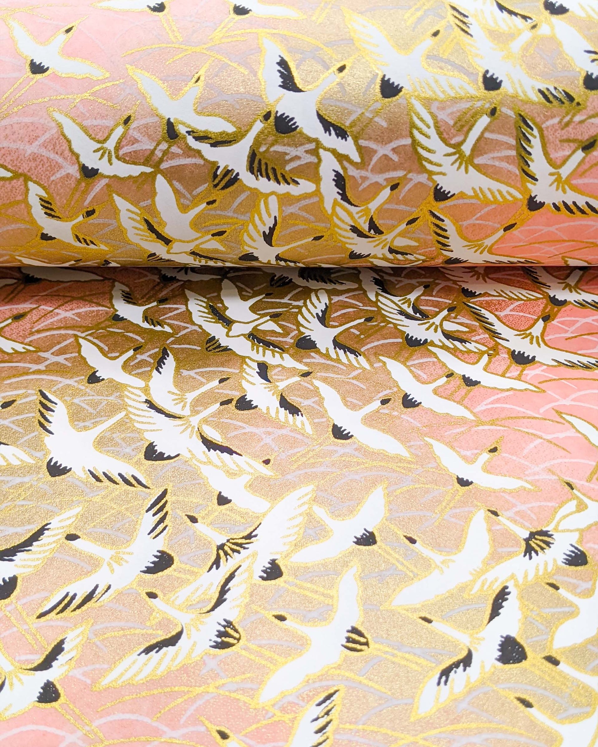 Japanese chiyogami paper featuring white flying cranes in a zigzag formation on a light pink background with metallic gold details.