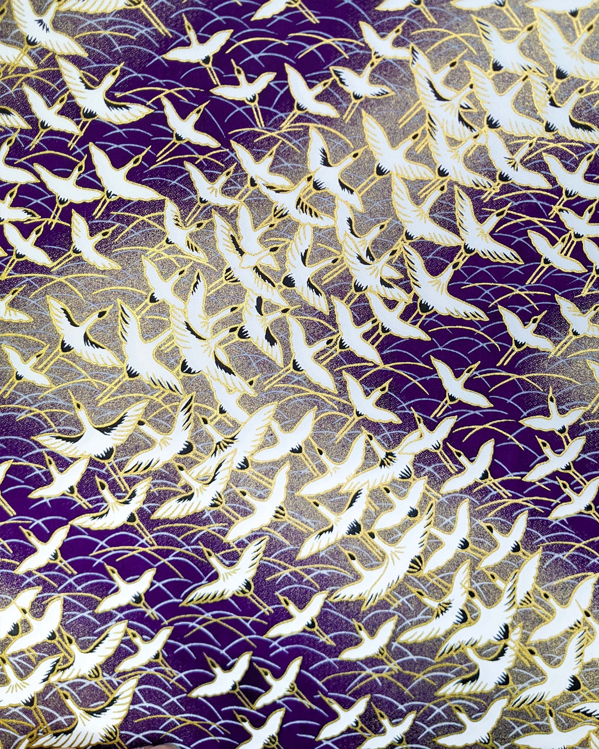 Japanese chiyogami paper featuring white flying cranes in a zigzag formation on a dark purple background with metallic gold details.