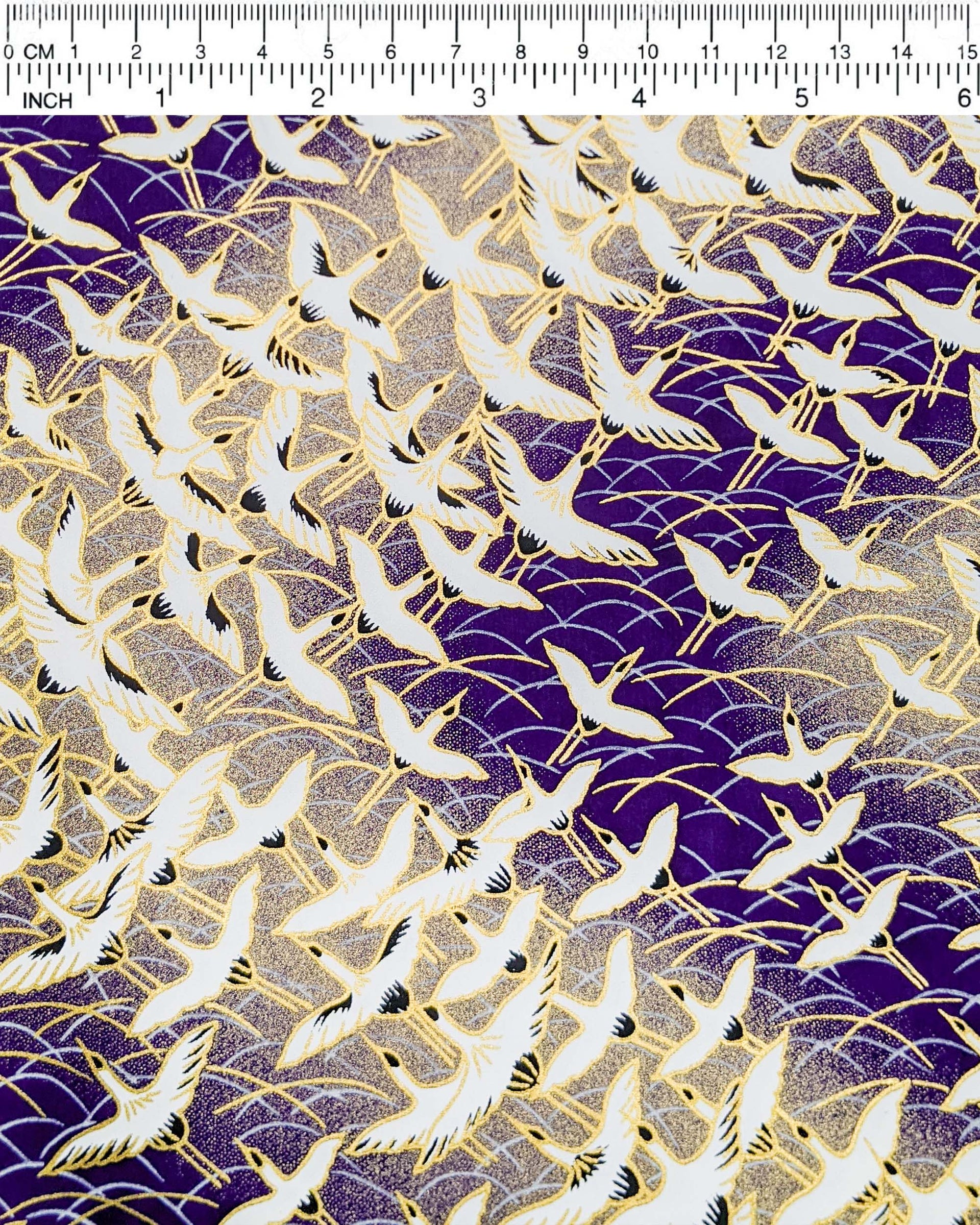 Japanese chiyogami paper featuring white flying cranes in a zigzag formation on a dark purple background with metallic gold details.