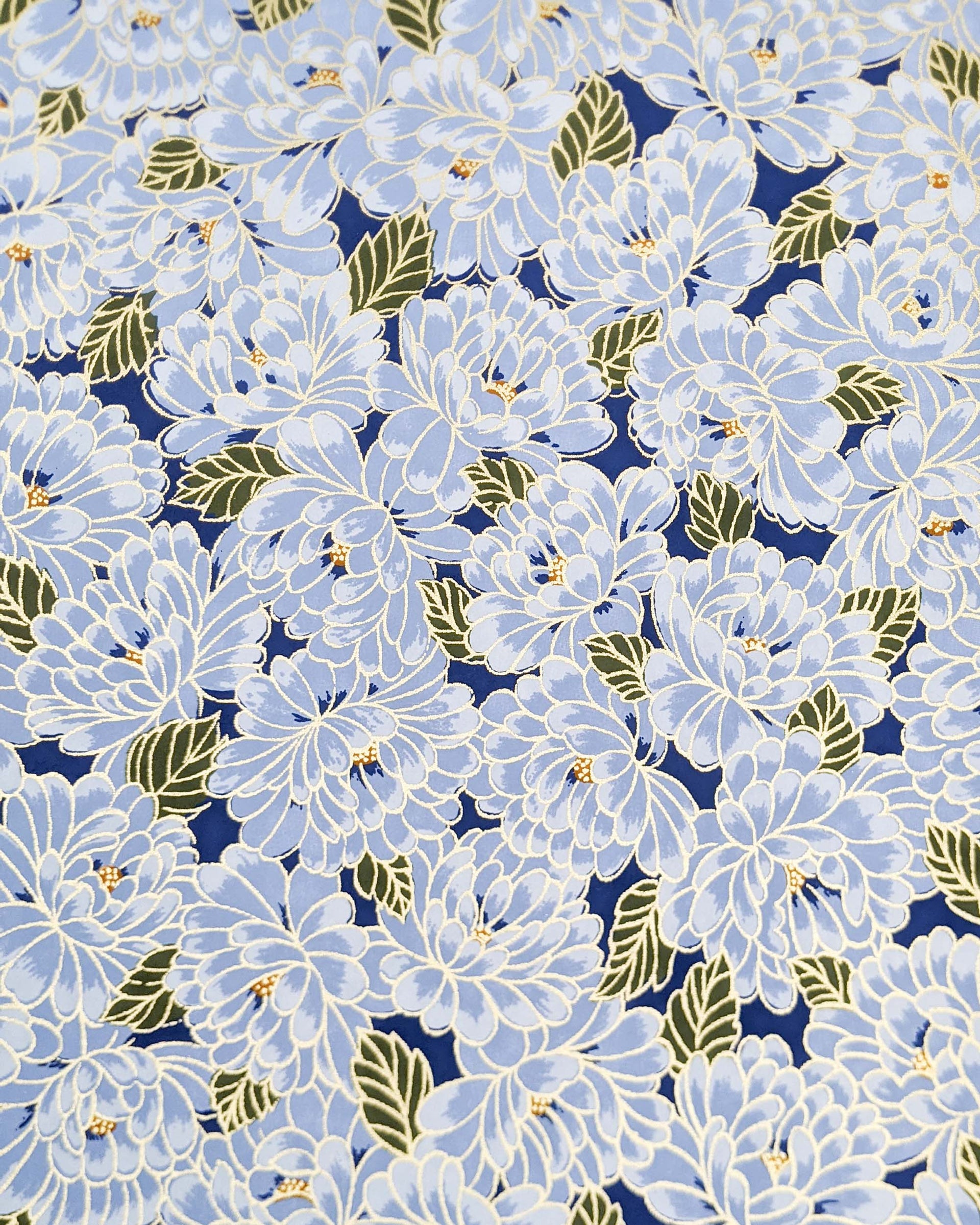 Japanese chiyogami paper featuring large light blue chrysanthemums with green leaves on a dark blue background with metallic gold details.