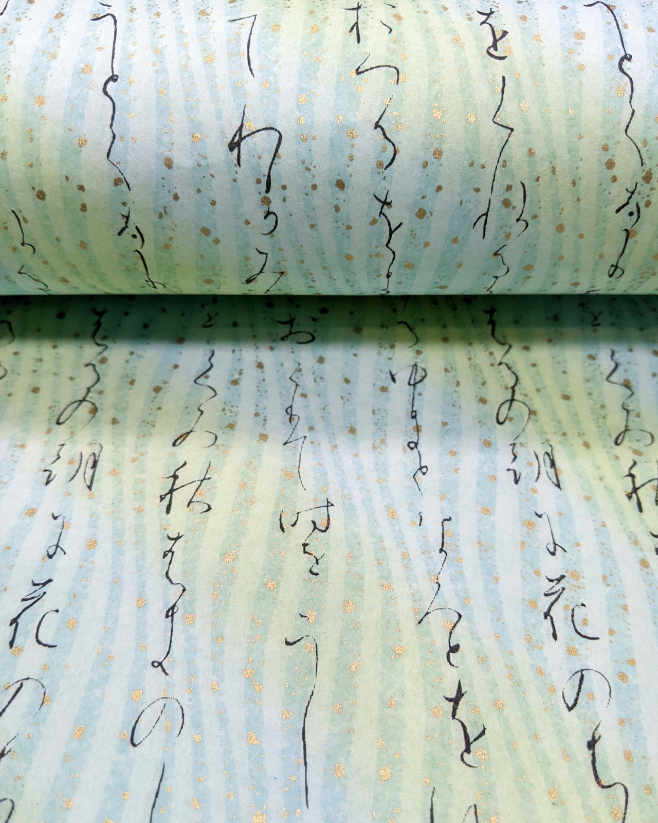 Japanese chiyogami paper featuring black Japanese calligraphy on a light turquoise background with metallic gold details.