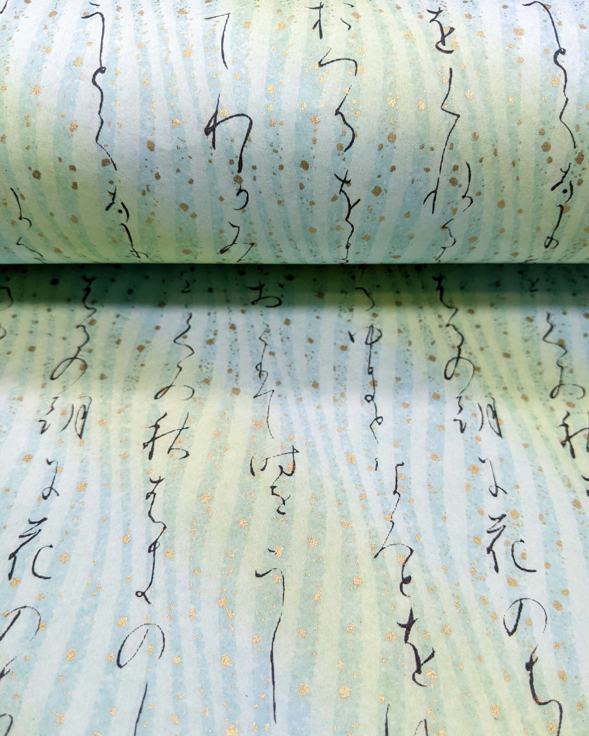 Japanese chiyogami paper featuring black Japanese calligraphy on a light turquoise background with metallic gold details.