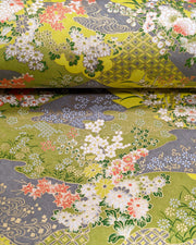 Japanese chiyogami paper featuring small white, green, and orange flowers on a gray and green background embedded with various traditional Japanese motifs with metallic gold details.