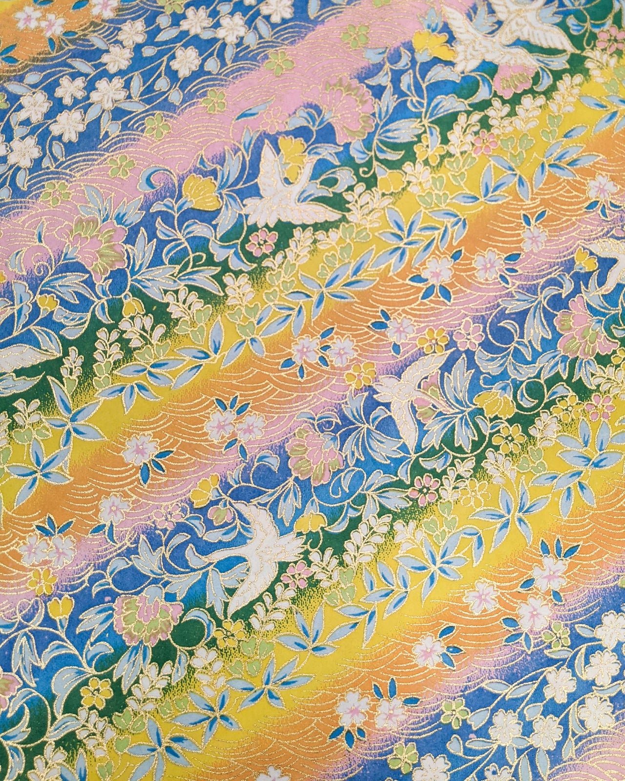 Japanese chiyogami paper featuring white cranes and a variety of flowers on a striped background in blue, pink, green, yellow, and orange with metallic gold details.