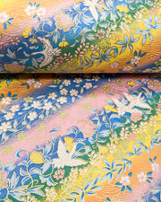 Japanese chiyogami paper featuring white cranes and a variety of flowers on a striped background in blue, pink, green, yellow, and orange with metallic gold details.
