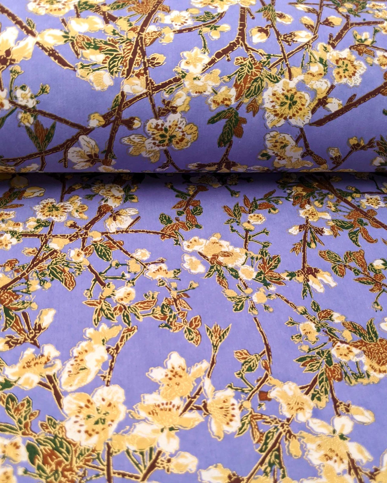 Japanese chiyogami paper featuring beige and white plum blossoms with dark brown branches and green leaves on a purple background with metallic gold details.