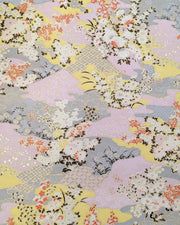 Japanese chiyogami paper featuring small white, black, and orange flowers on a pink, beige, and purple background embedded with various traditional Japanese motifs with metallic gold details.