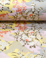 Japanese chiyogami paper featuring small white, black, and orange flowers on a pink, beige, and purple background embedded with various traditional Japanese motifs with metallic gold details.
