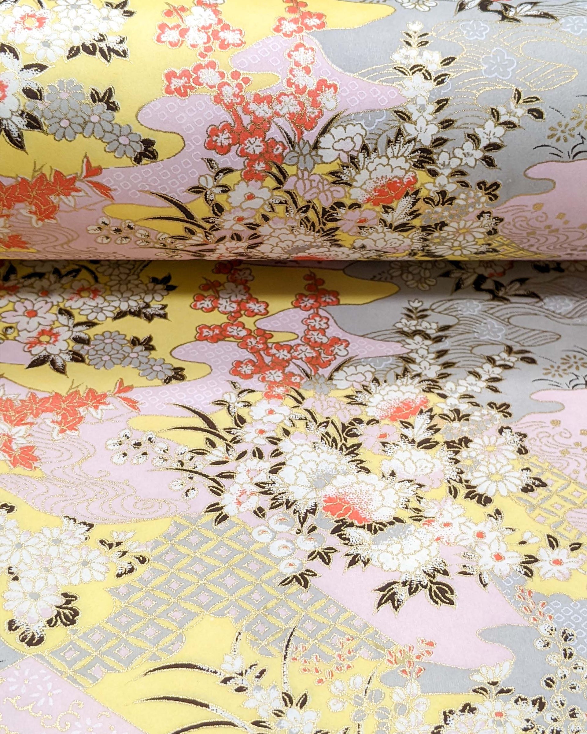 Japanese chiyogami paper featuring small white, black, and orange flowers on a pink, beige, and purple background embedded with various traditional Japanese motifs with metallic gold details.