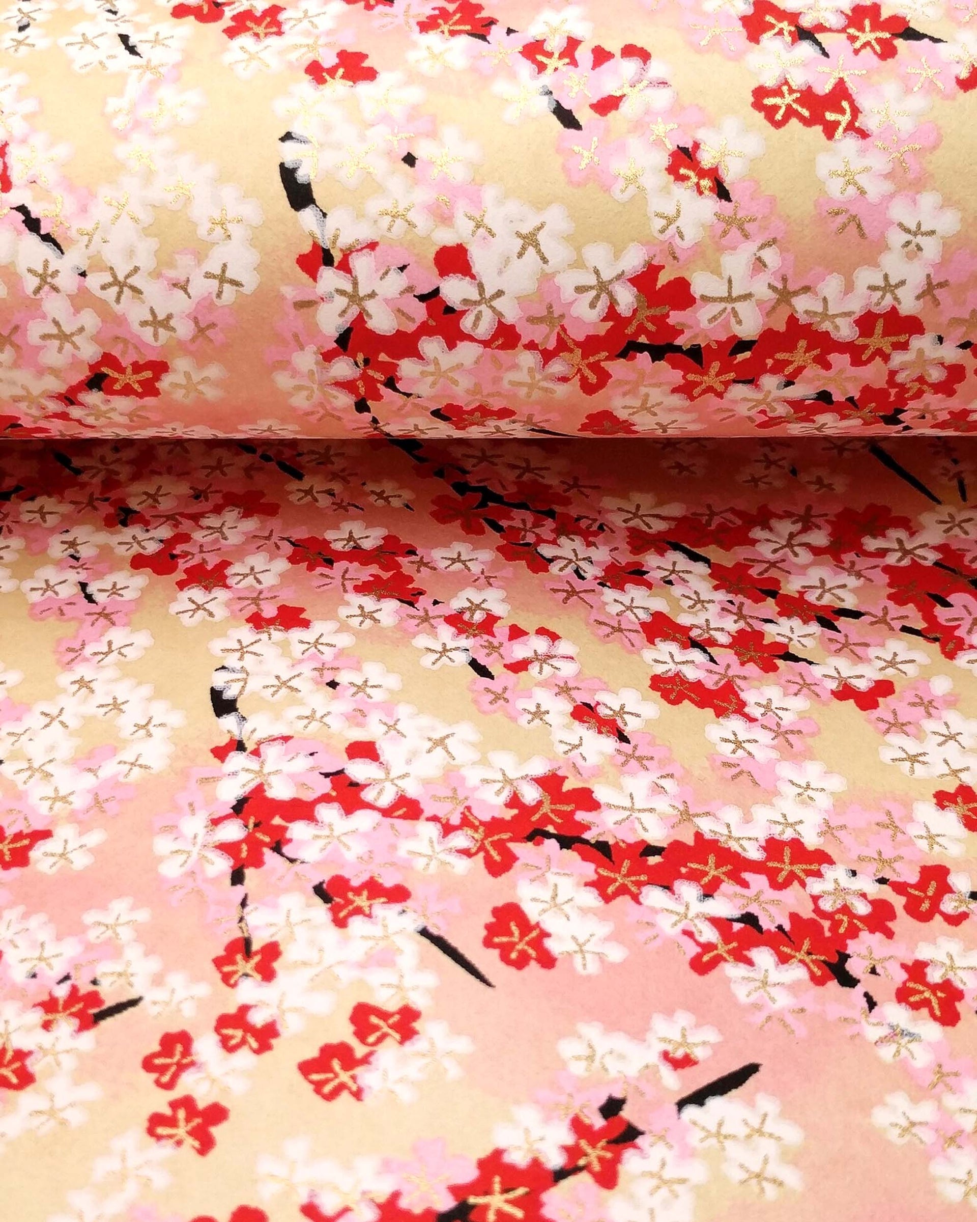 Japanese chiyogami paper featuring pink, red, and white cherry blossoms on a pink and beige background with metallic gold details.