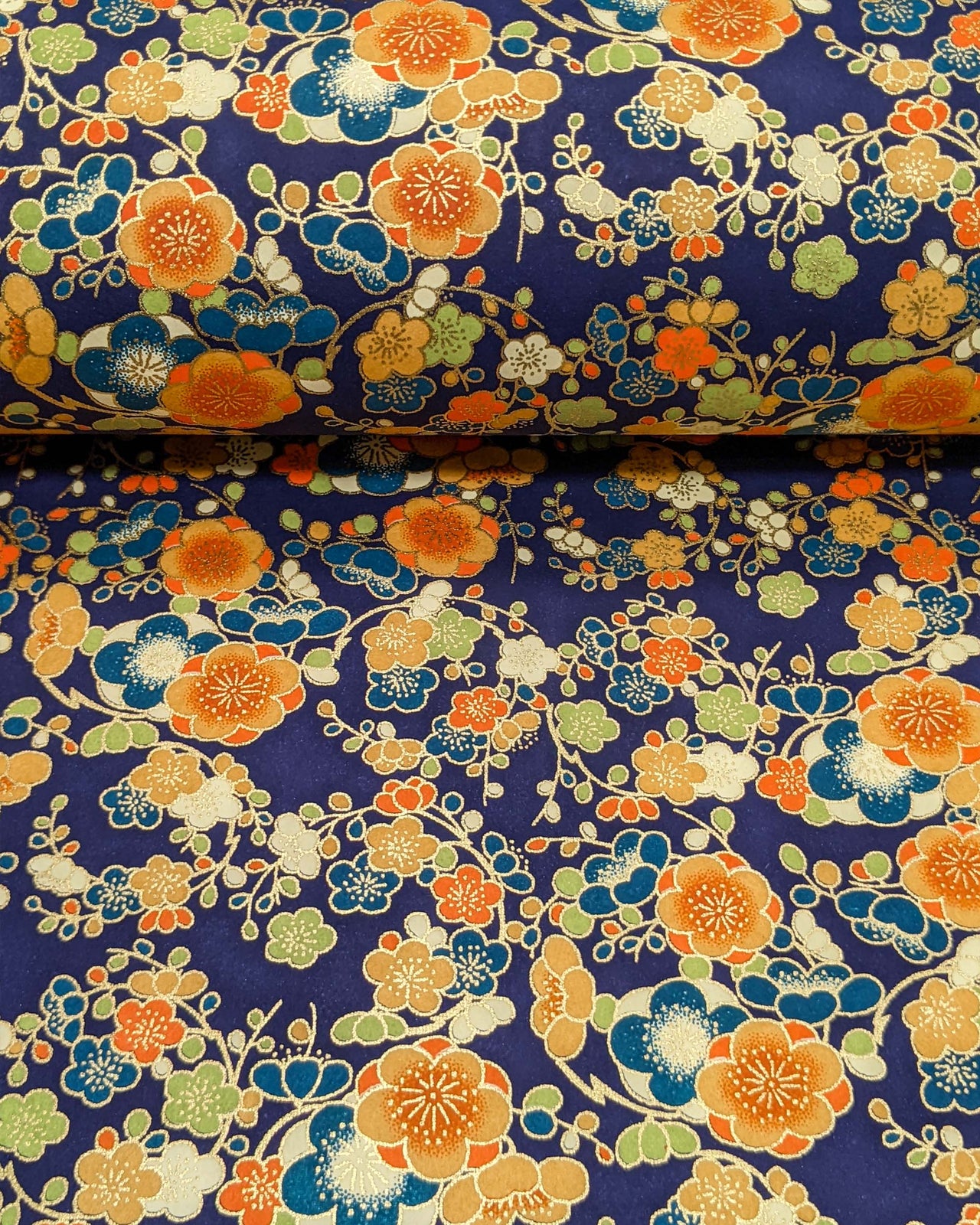 Japanese chiyogami paper featuring orange, blue, green, and cream plum blossoms on a dark blue background with metallic gold details.