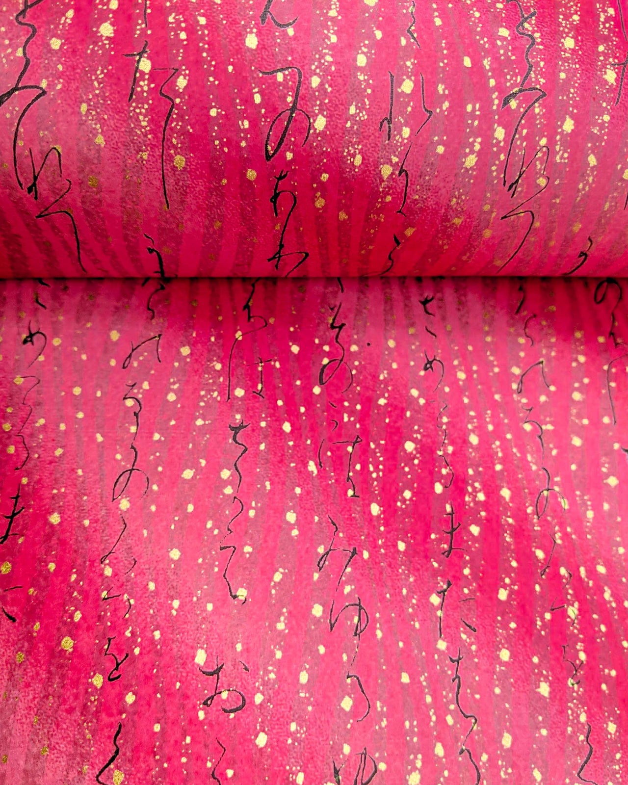 Japanese chiyogami paper featuring black kanji calligraphy on a pink vertical swirl background with metallic gold details.