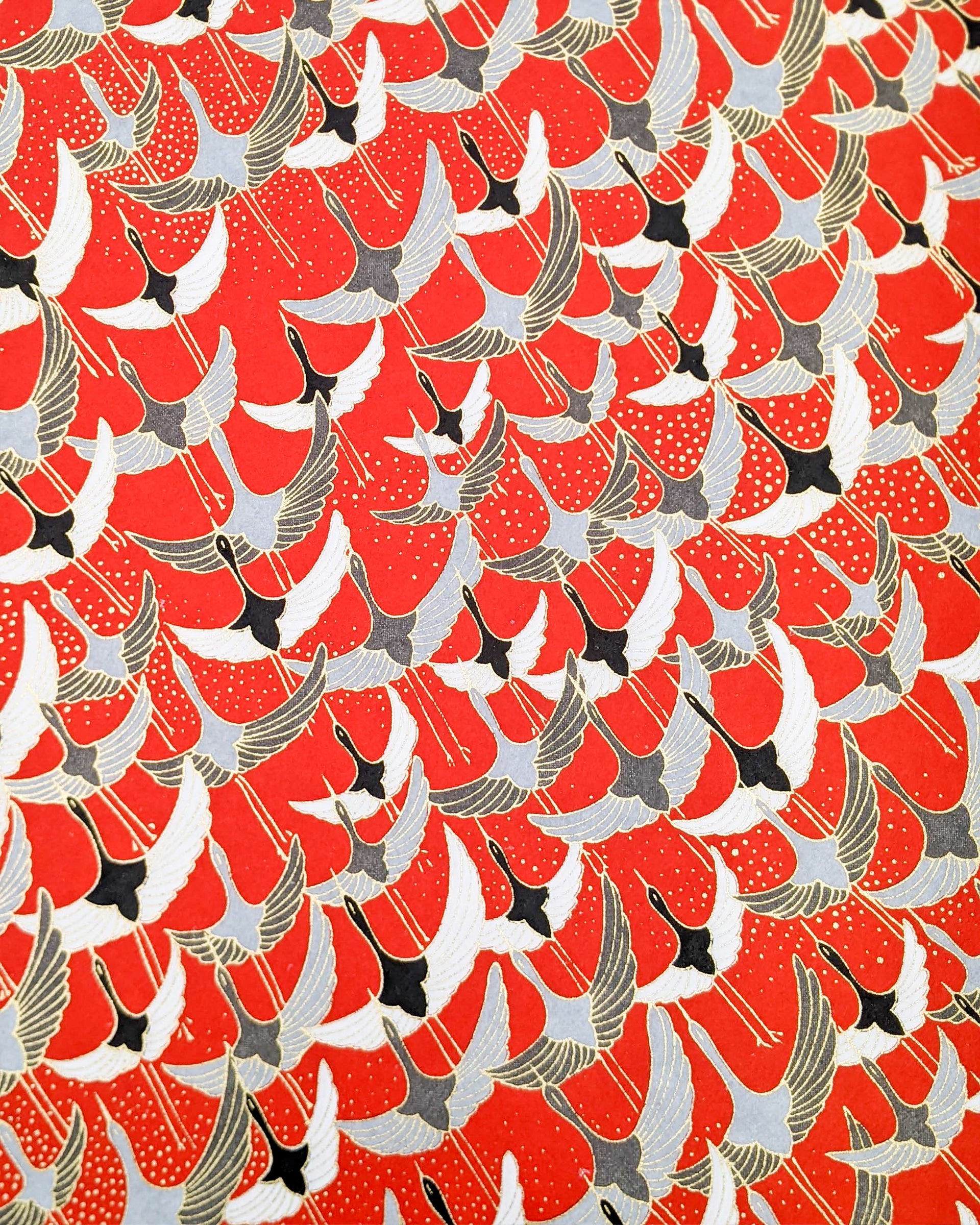 Japanese chiyogami paper featuring gray, black, and white flying cranes on a red background with metallic gold details. 