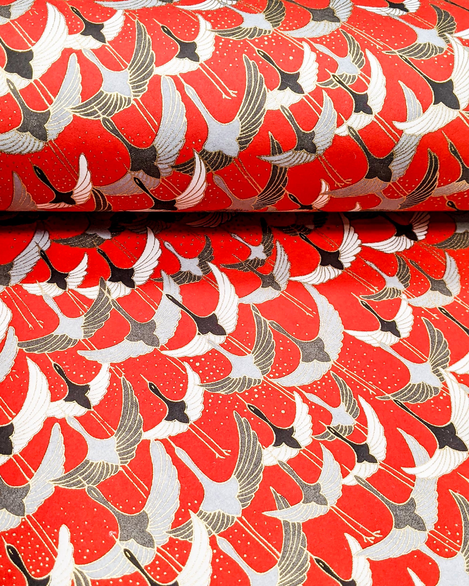 Japanese chiyogami paper featuring gray, black, and white flying cranes on a red background with metallic gold details. 